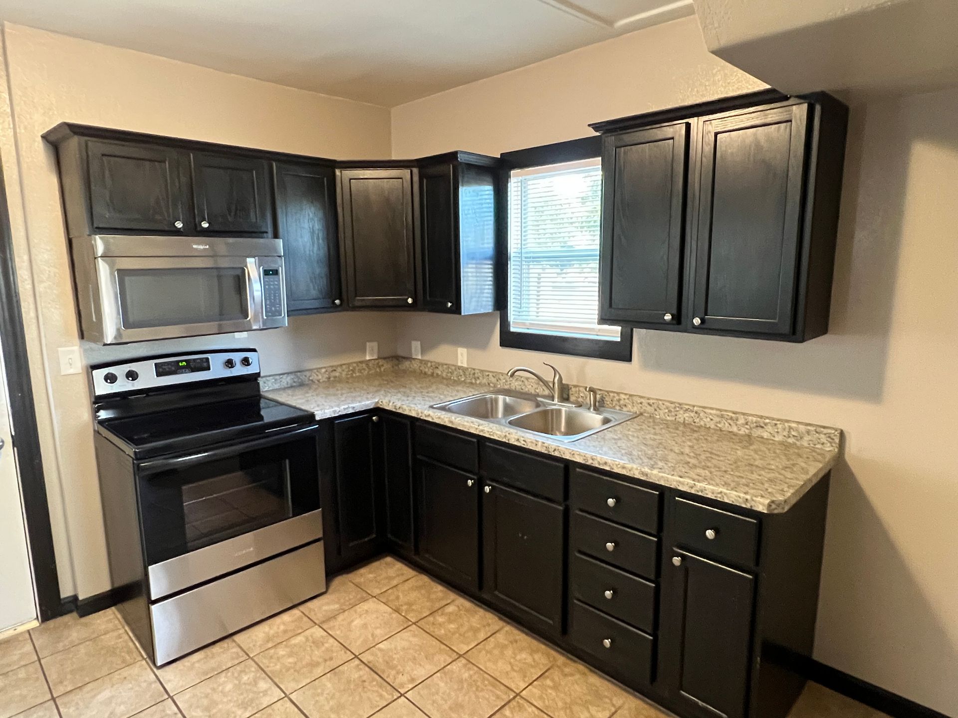 A kitchen with black cabinets , a stove , a sink , and a microwave.