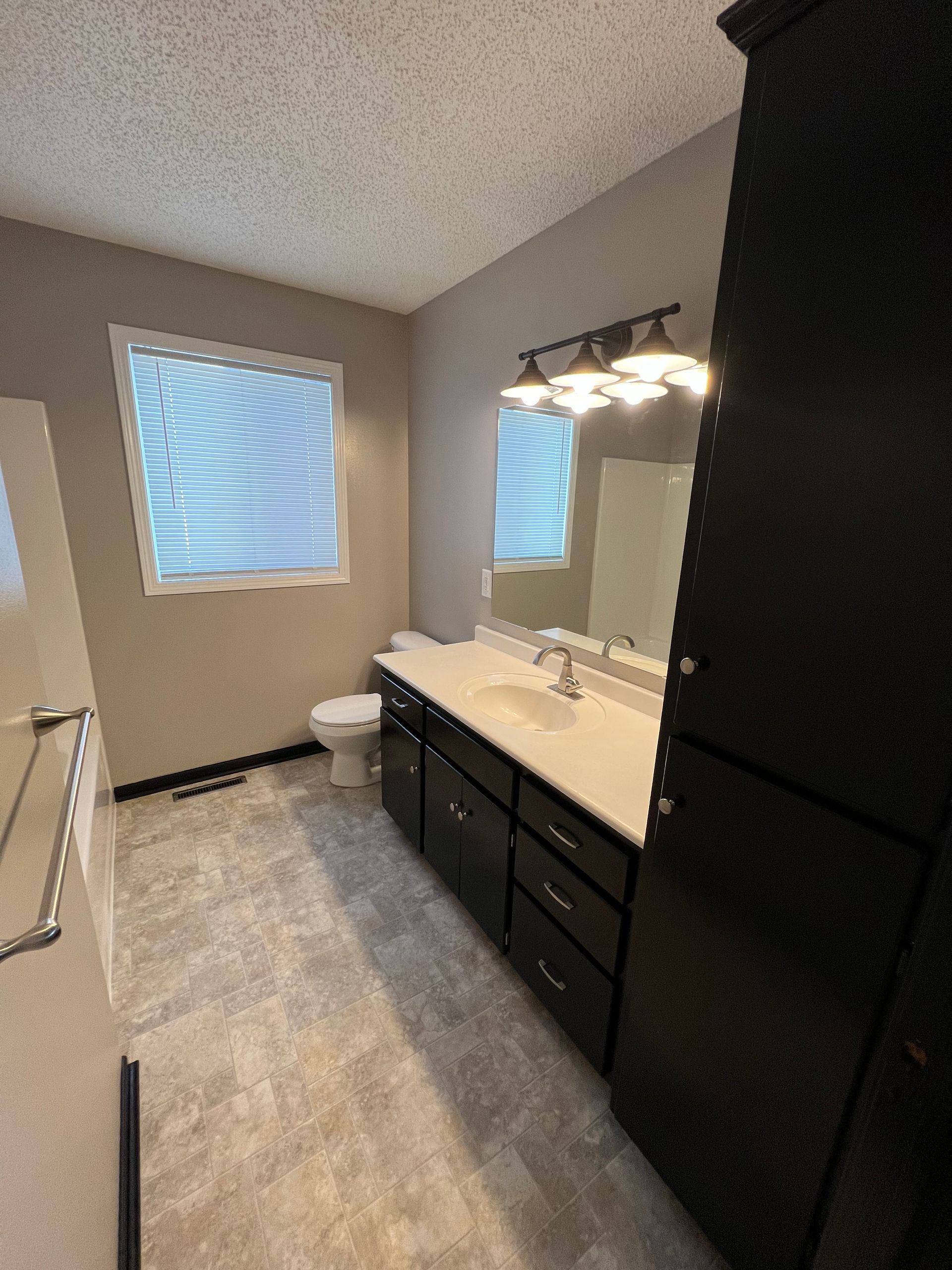 A bathroom with a toilet , sink , mirror and cabinets.