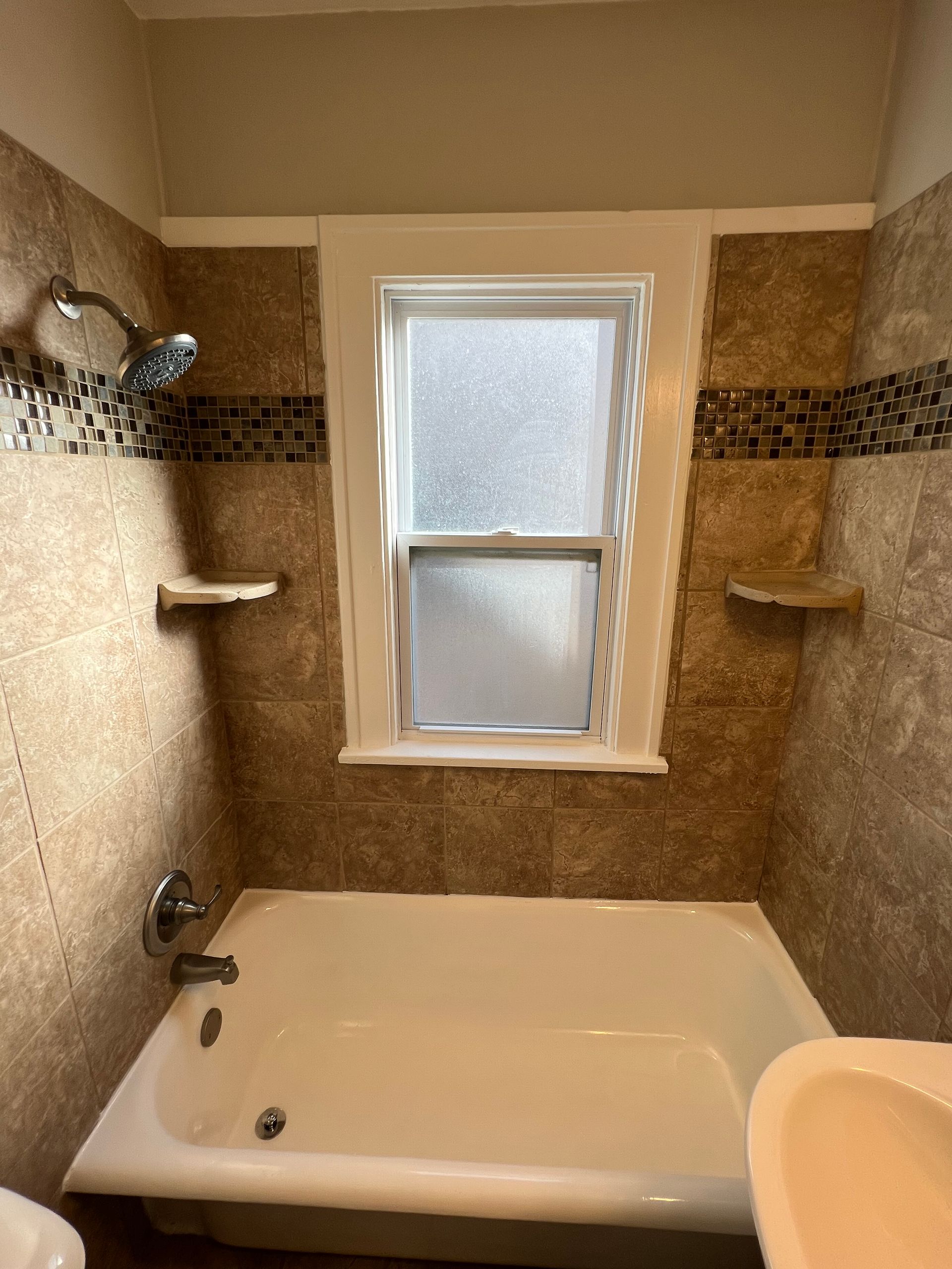 A bathroom with a tub , sink , shower and window.