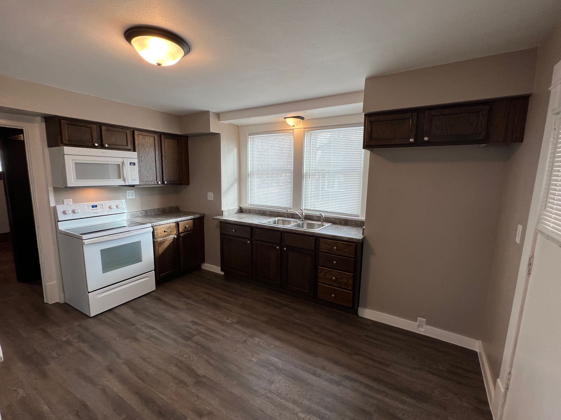 An empty kitchen with a stove , microwave , sink and cabinets.