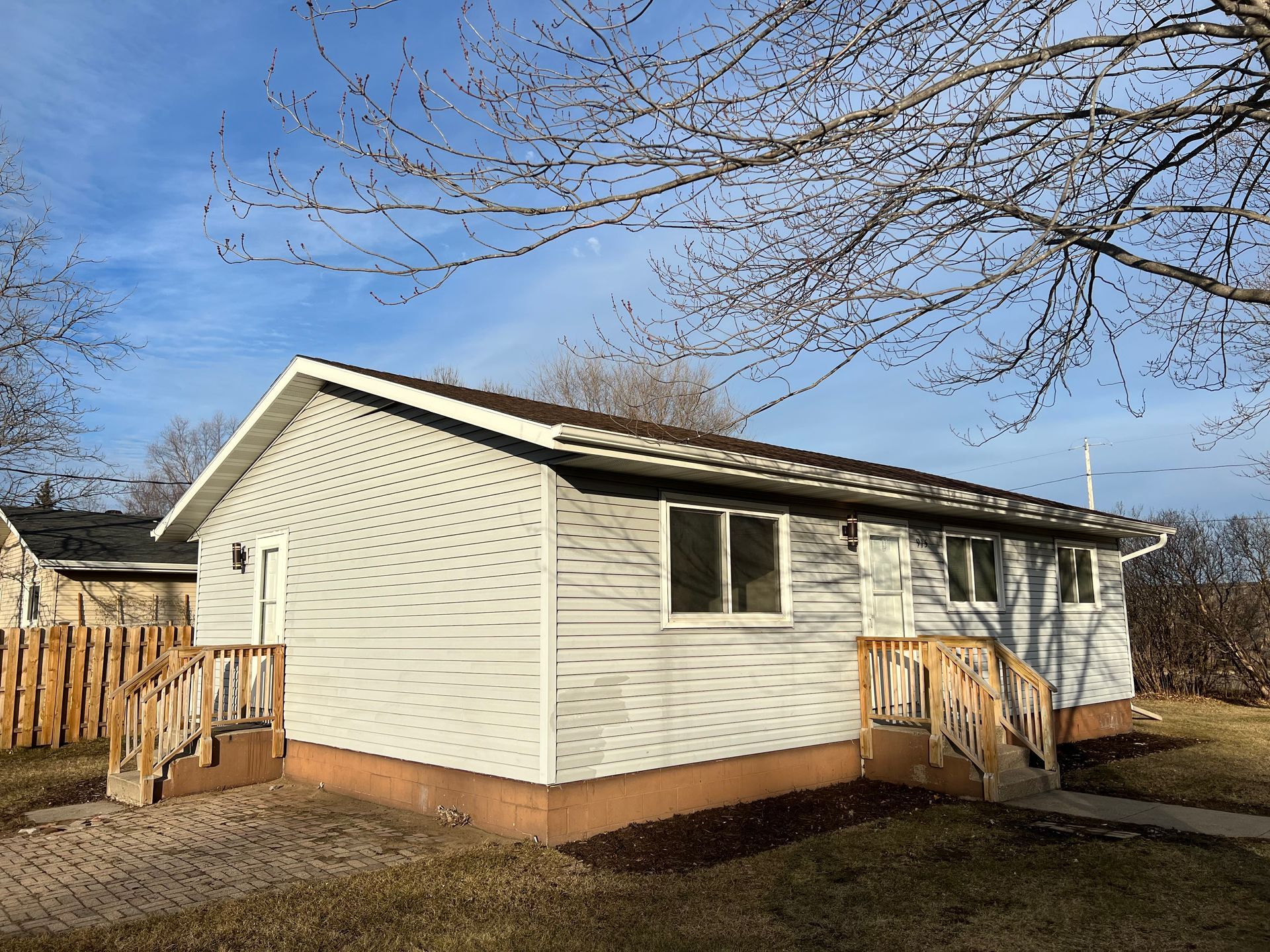 A small white house with a wooden deck and stairs.