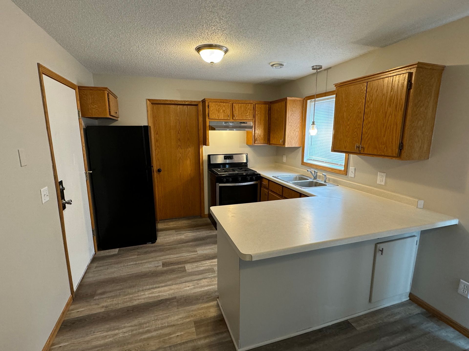 A kitchen with wooden cabinets , a black refrigerator , a stove and a sink.