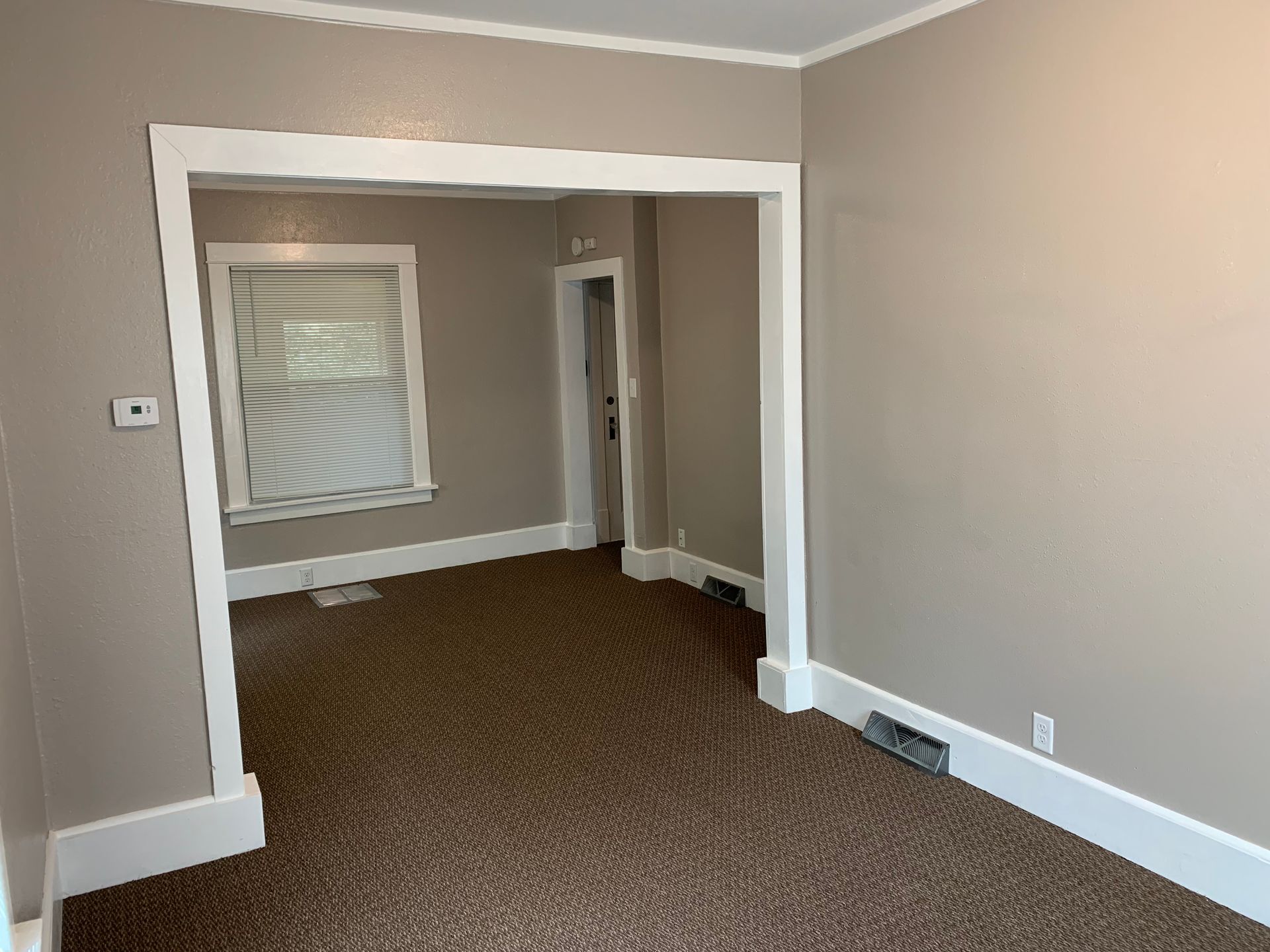 An empty living room with a window and brown carpet.