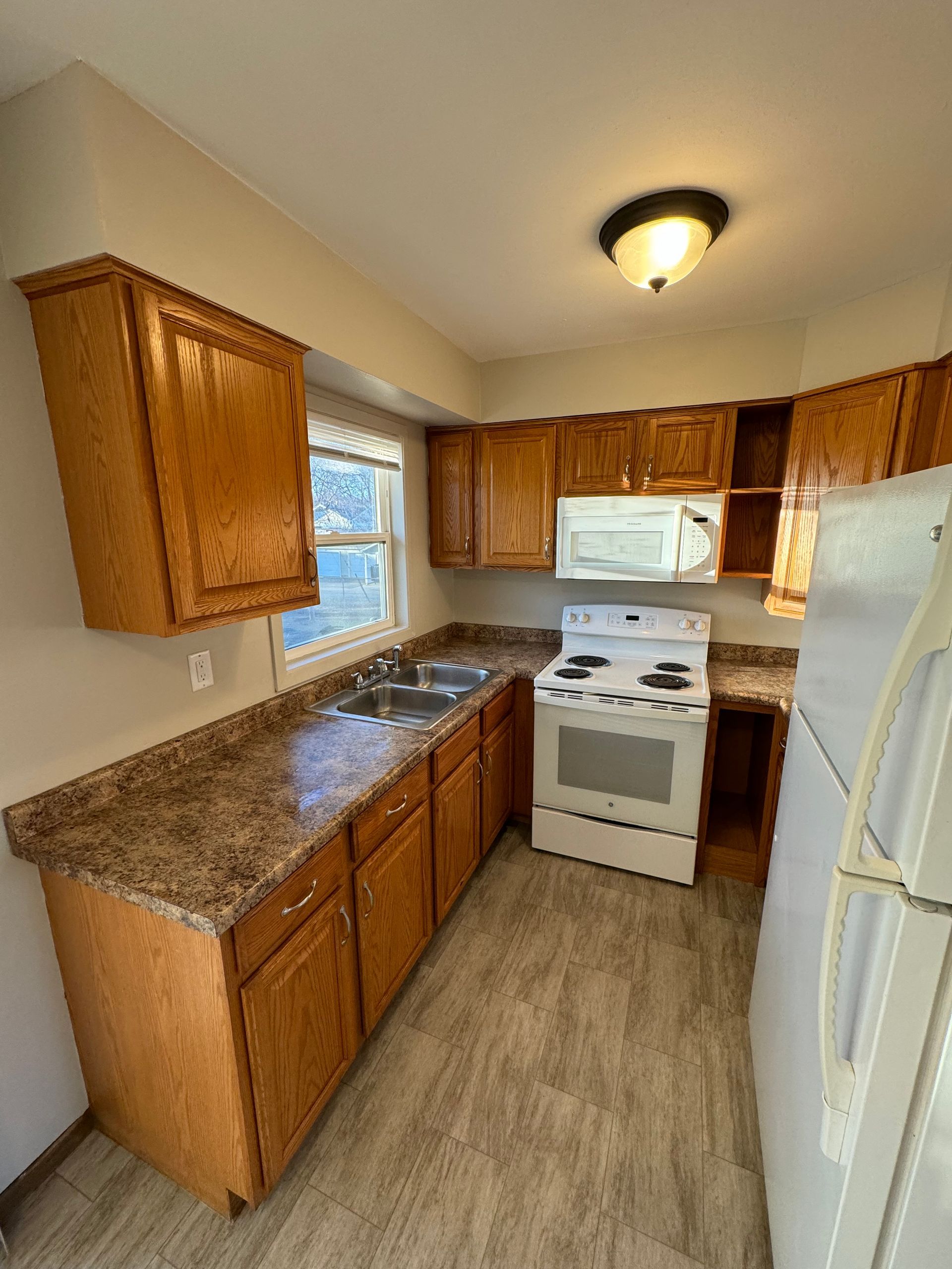 A kitchen with a stove , refrigerator , microwave and sink.