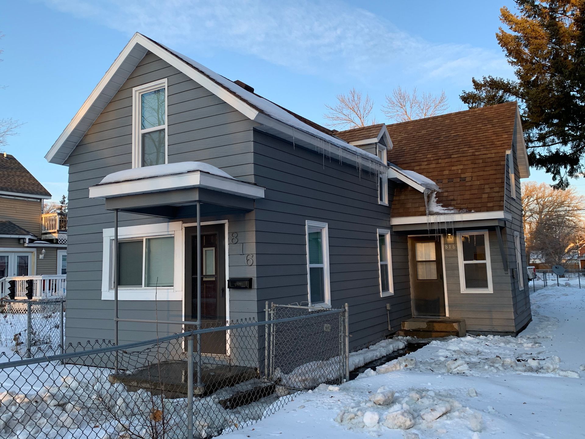 A gray house with a brown roof is surrounded by snow