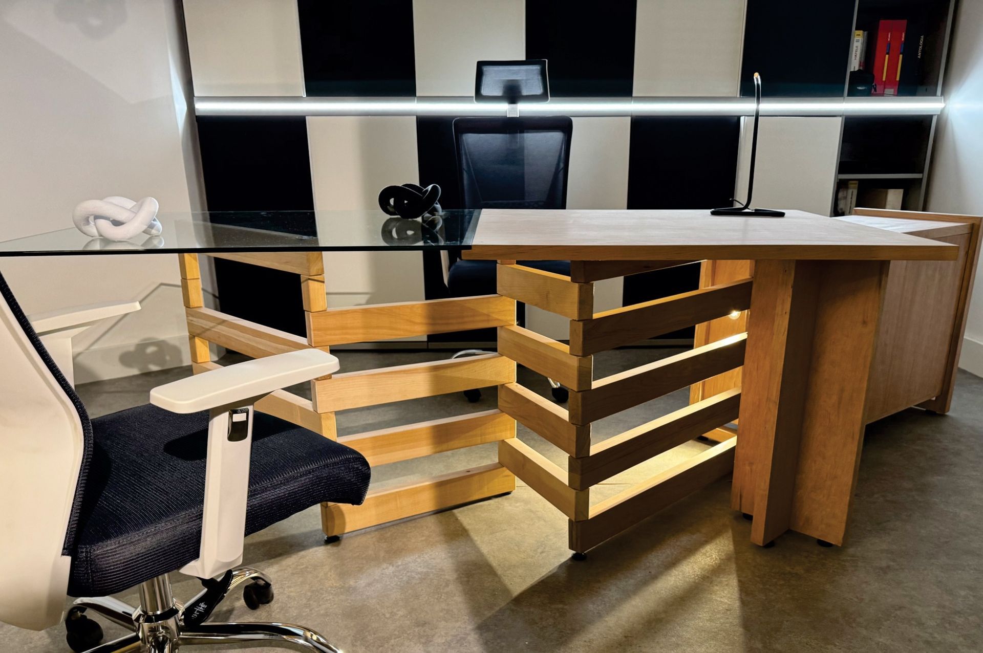 Escritorio de oficina moderno con estantes de madera, silla negra y monitor de computadora al fondo.