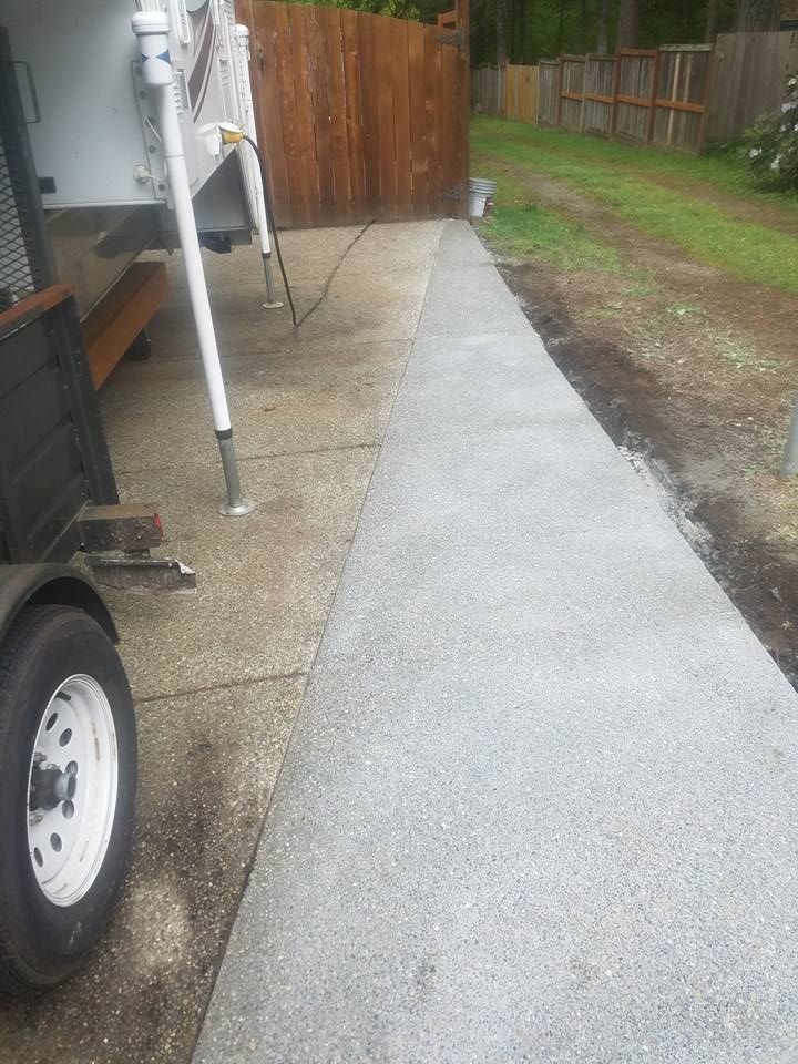 Exposed aggregate concrete walkway installed alongside RV parking pad with clean edge finish and broomed border detail