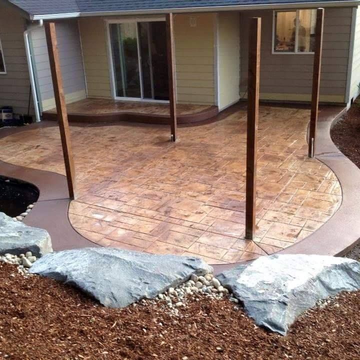 Backyard concrete patio design with decorative rock landscaping and stamped surface