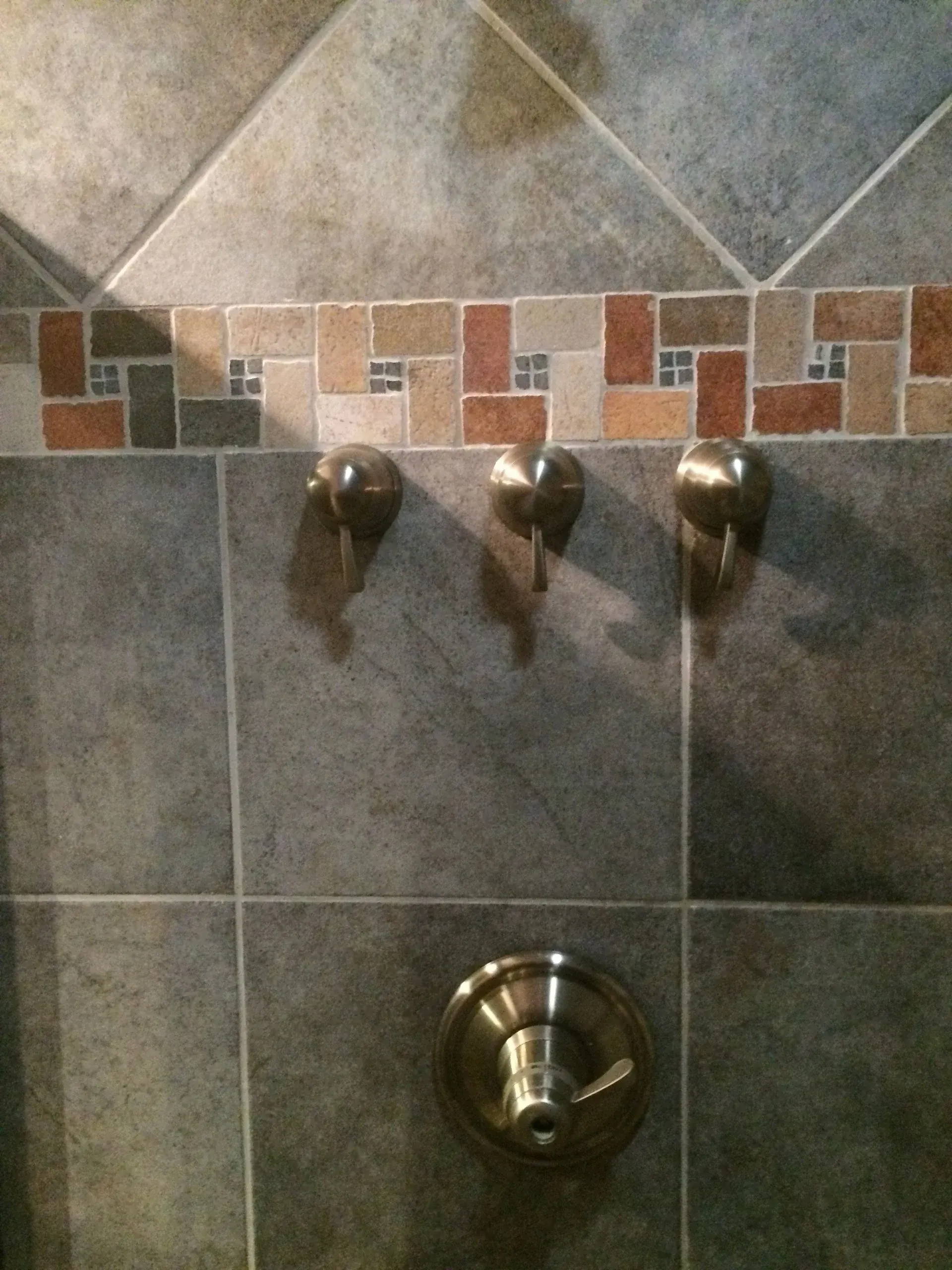 Shower wall with three metal hooks and a chrome knob on gray tiled background.