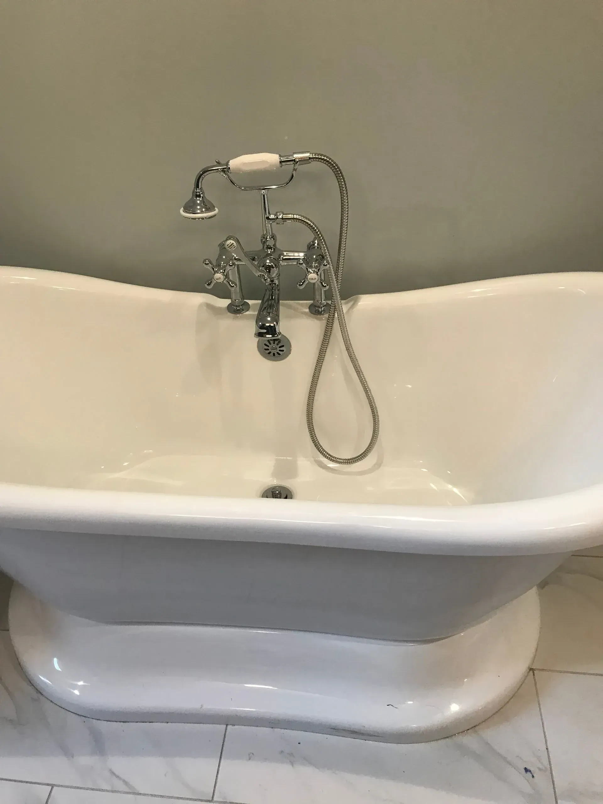 White freestanding bathtub with chrome faucet and handheld shower against a beige wall