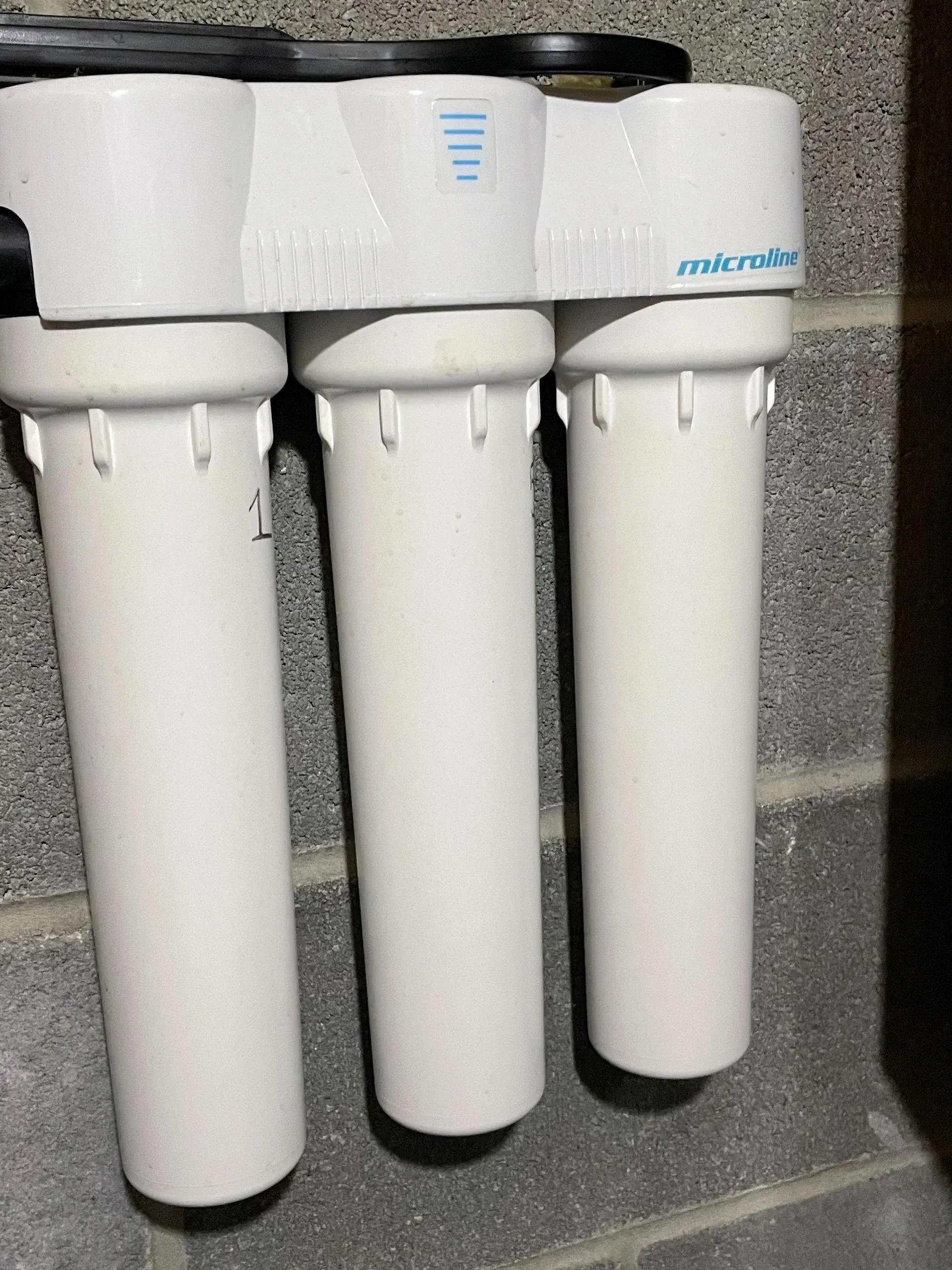 Three white water filter cartridges mounted under a sink on a countertop.