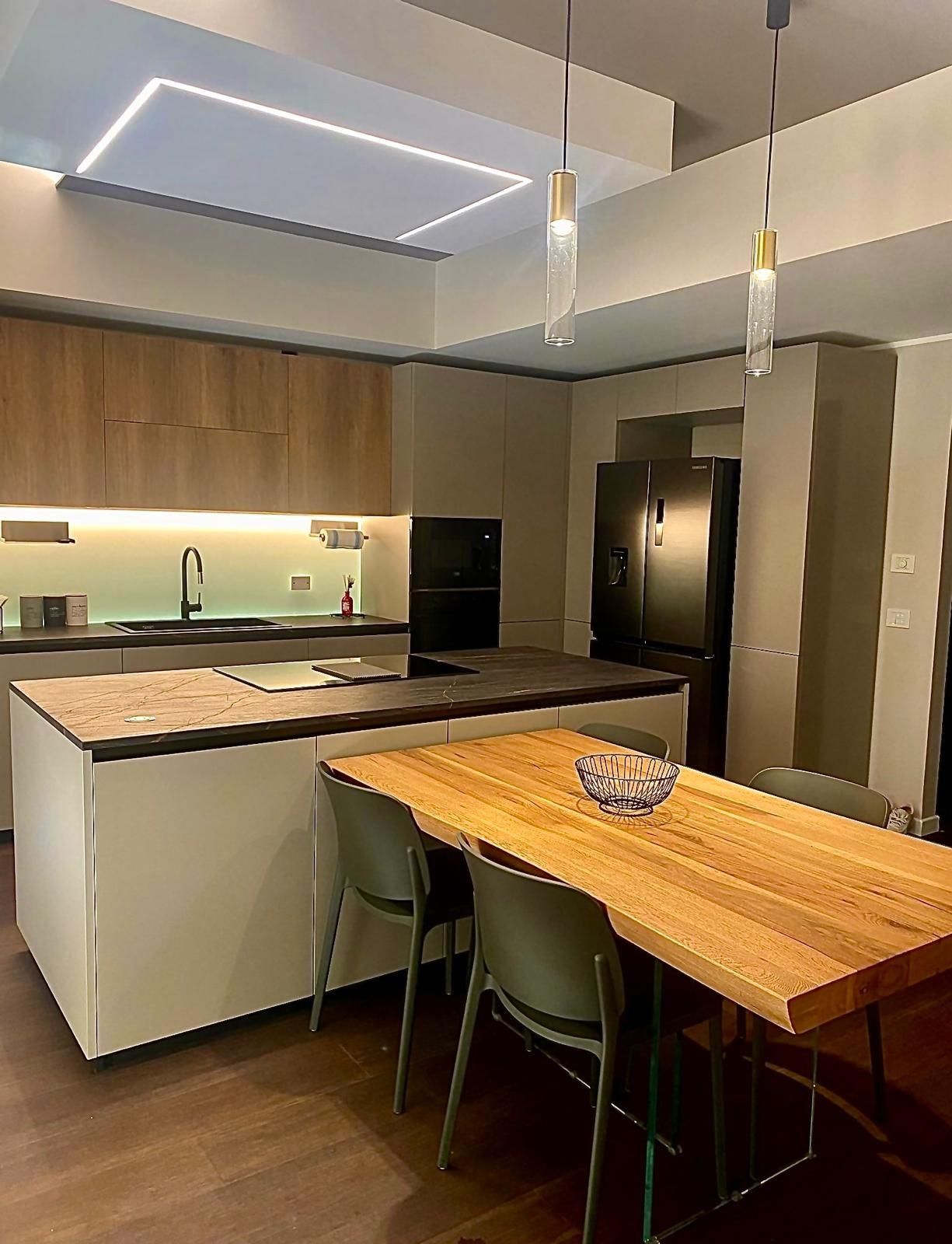 Cucina moderna con tavolo in legno, isola in marmo, sedie verdi e lampade a sospensione in un interno elegante.
