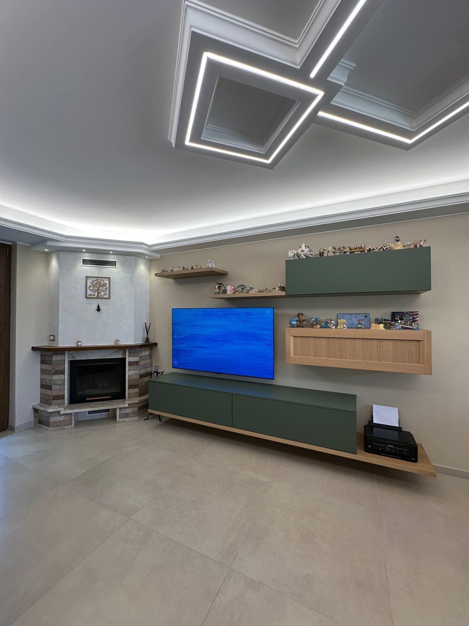 Soggiorno moderno con lampade a soffitto geometriche, TV a parete, camino e mobili sospesi verdi.