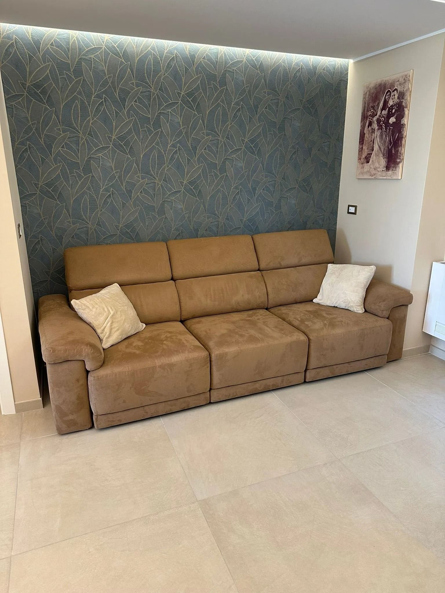 In un luminoso soggiorno, un divano beige con cuscini decorativi è posizionato contro una parete color verde acqua.