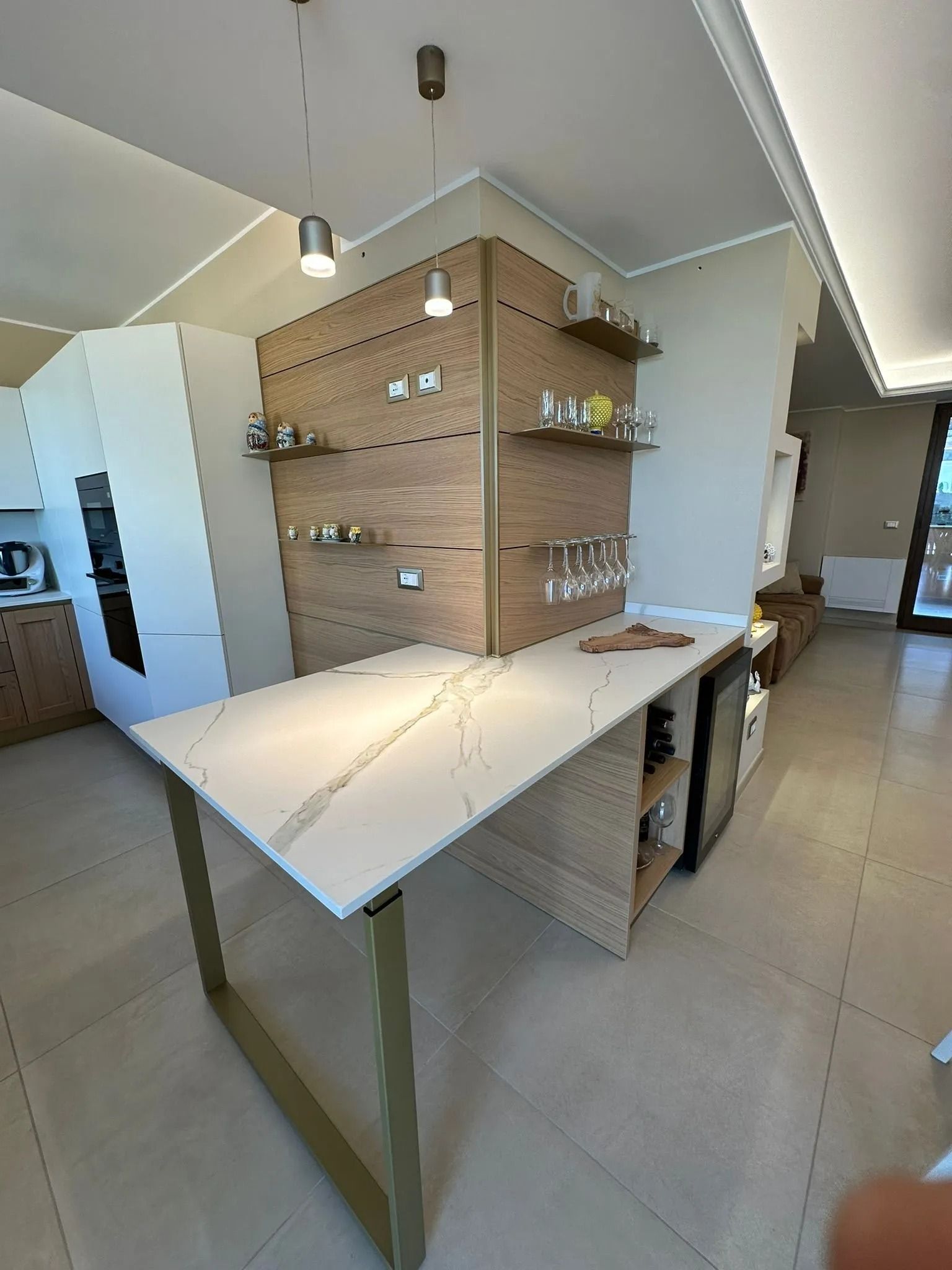 Interno moderno di una caffetteria con bancone bianco, scaffali in legno, lampade a sospensione e pavimento piastrellato.