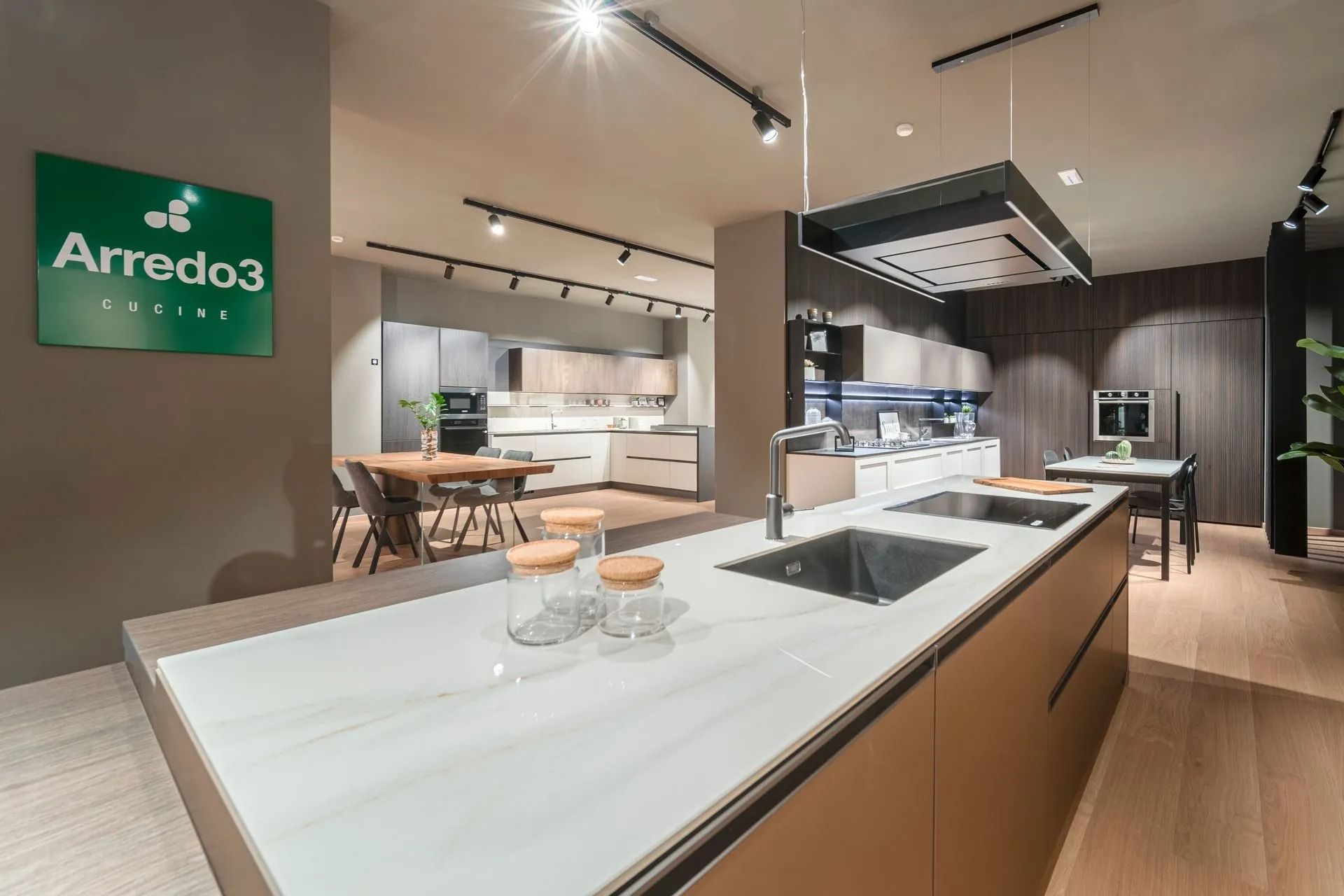 Showroom di cucine moderne con isola bianca, mobili in legno e zona pranzo.