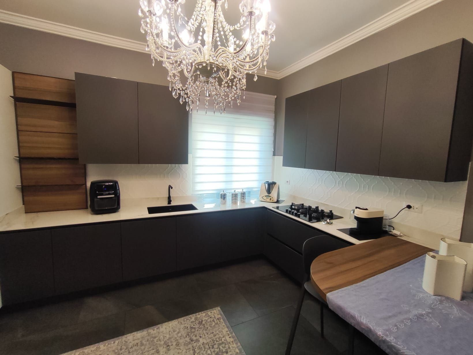 Cucina moderna con mobili scuri, lampadario, lavello, piano cottura e finestra sopra il bancone.