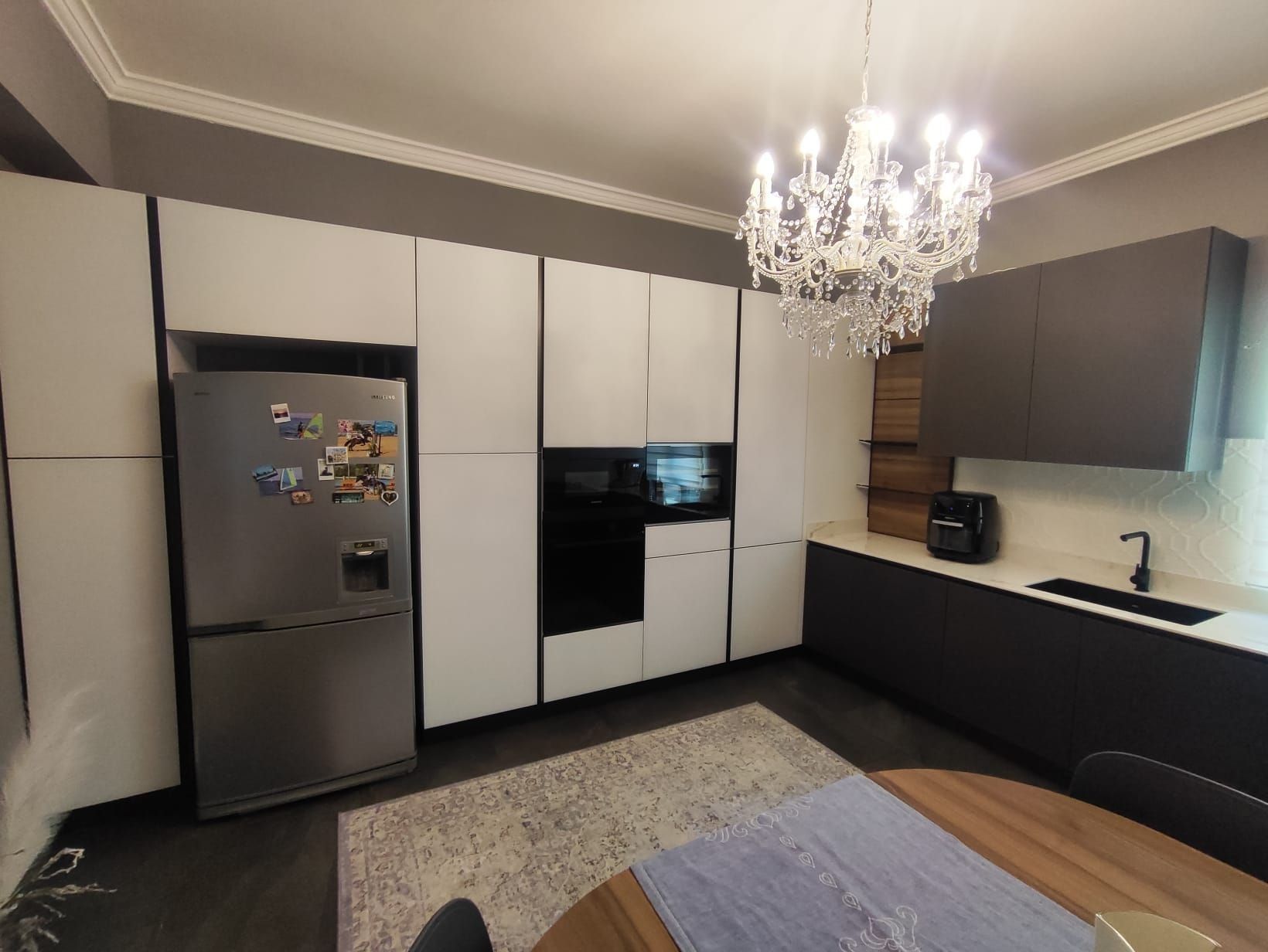 Cucina moderna con mobili bianchi, ripiani neri, frigorifero in acciaio inox e lampadario