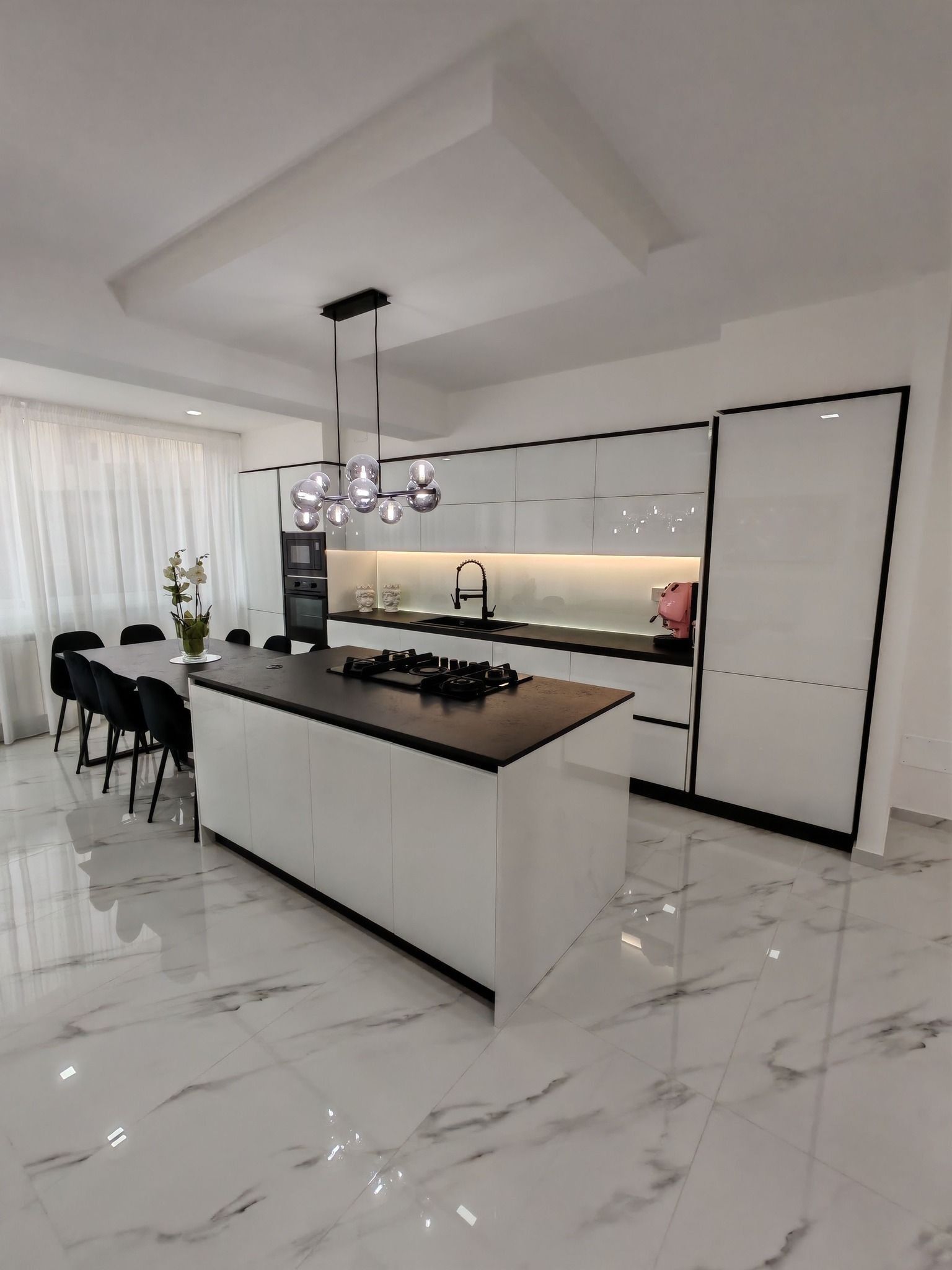Cucina moderna bianca con pavimento in marmo, isola centrale, lampada a sospensione e sgabelli da bar.