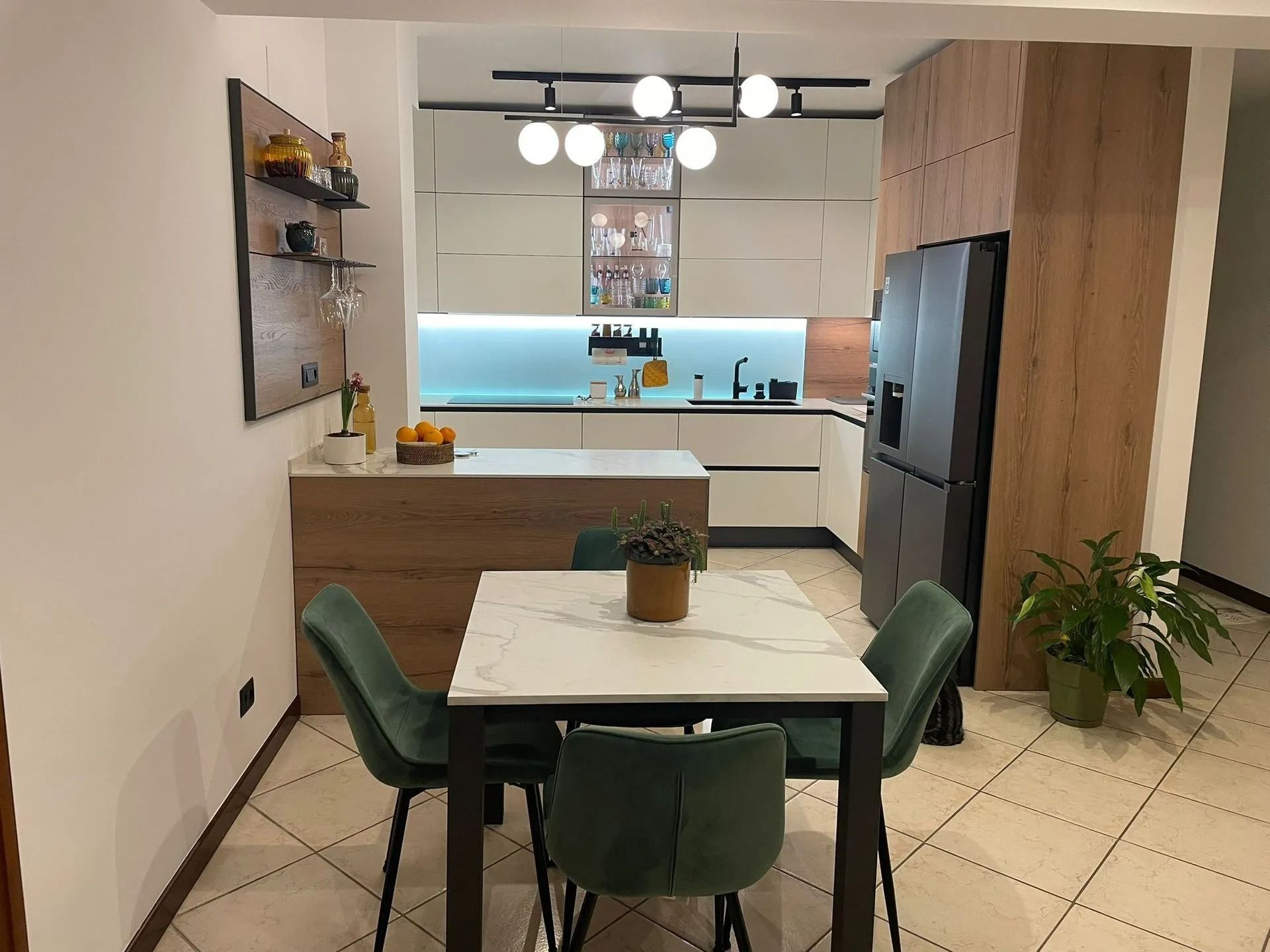 Cucina e zona pranzo moderne con sedie verdi, tavolo bianco, mobili in legno e un luminoso paraschizzi blu.