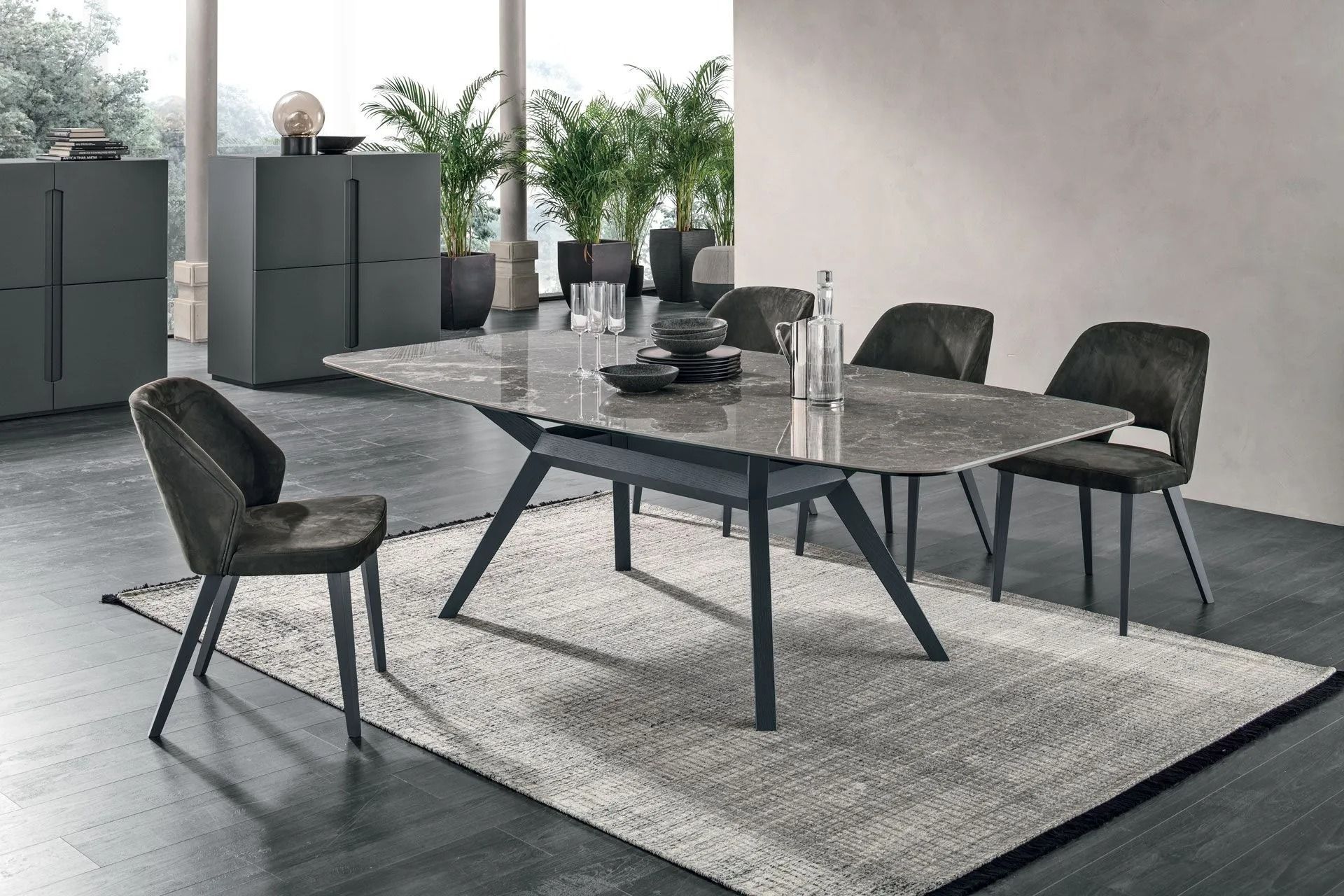 Sala da pranzo moderna con tavolo in marmo grigio, quattro sedie e un tappeto chiaro vicino alle finestre.