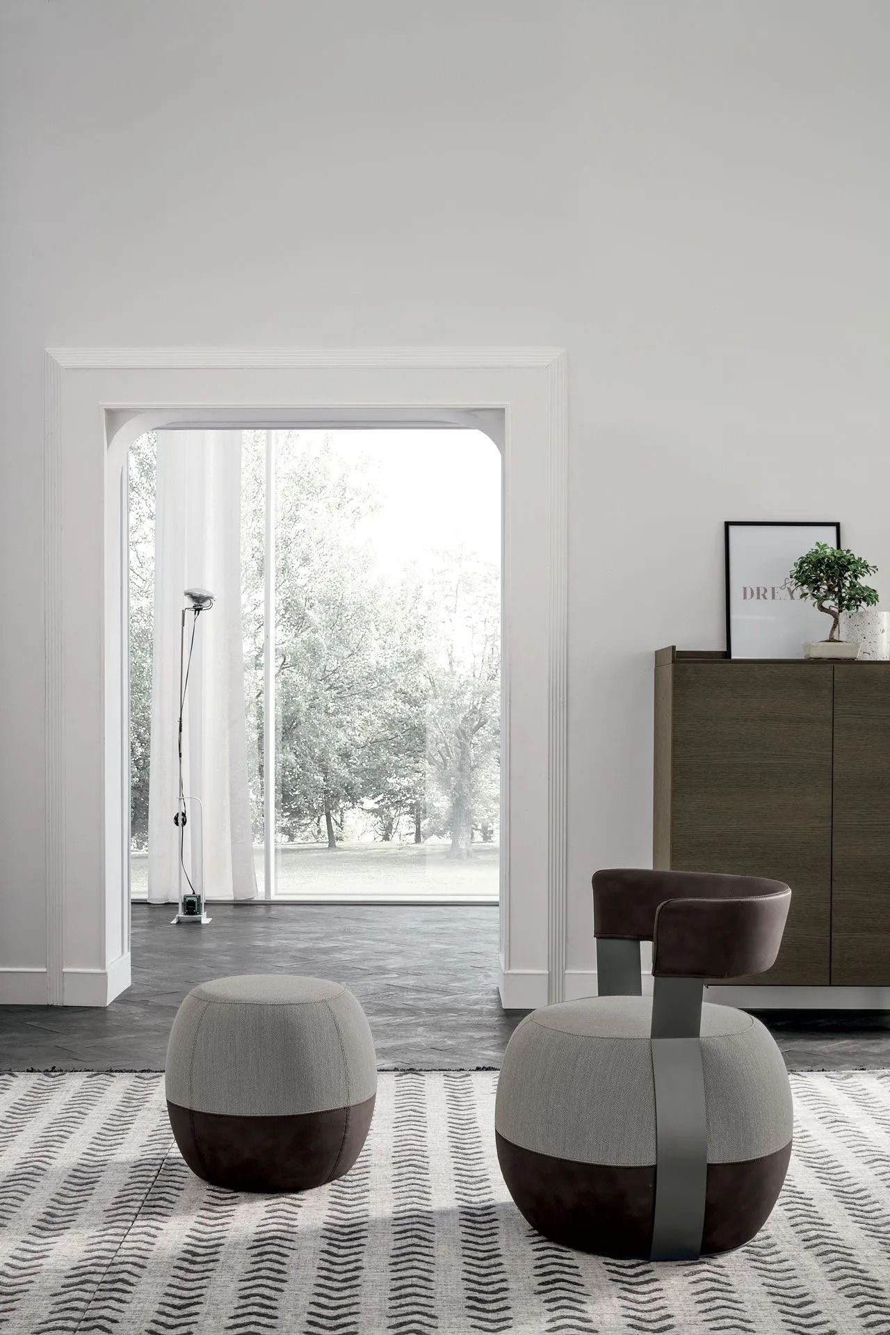 Soggiorno moderno con due pouf imbottiti, tappeto a motivi geometrici e porta che conduce a un luminoso patio.