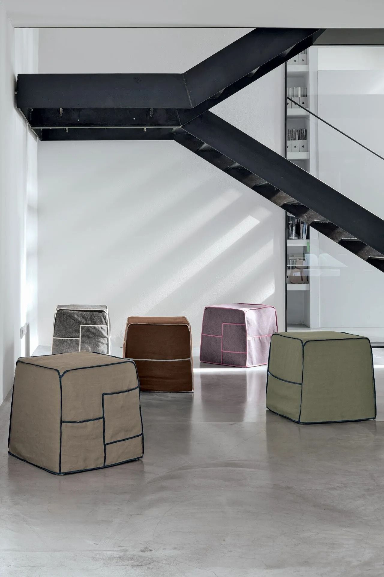 Stanza moderna con scala nera e quattro sedute a cubo nei colori beige, marrone, rosa e verde salvia.