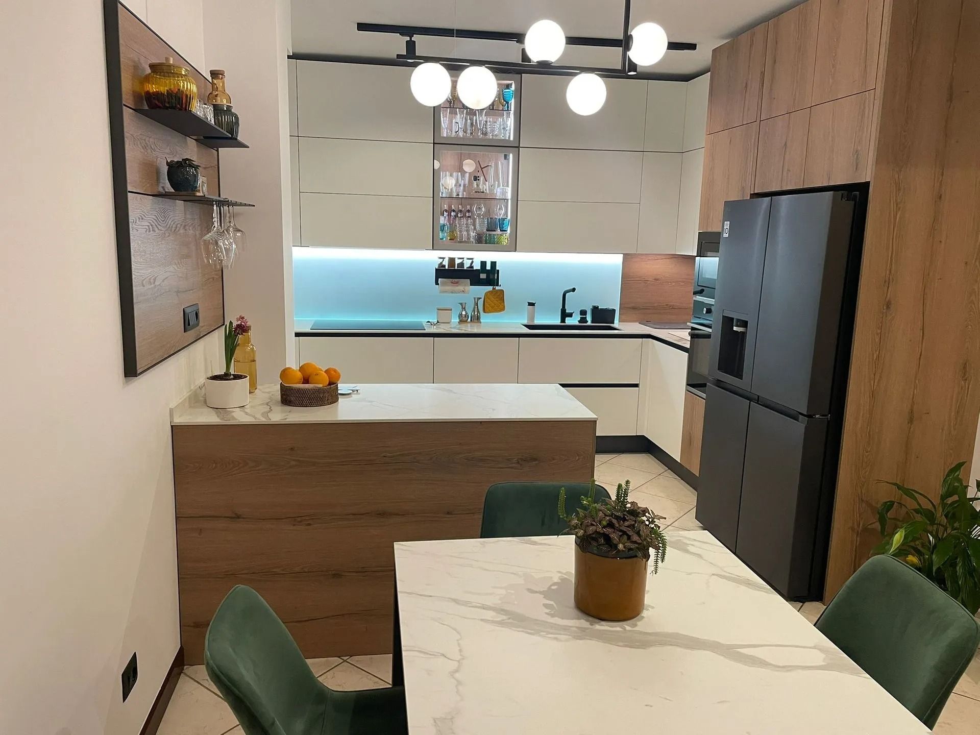Cucina moderna e zona pranzo con isola bianca, sedie verdi, frigorifero nero e lampade a sospensione.