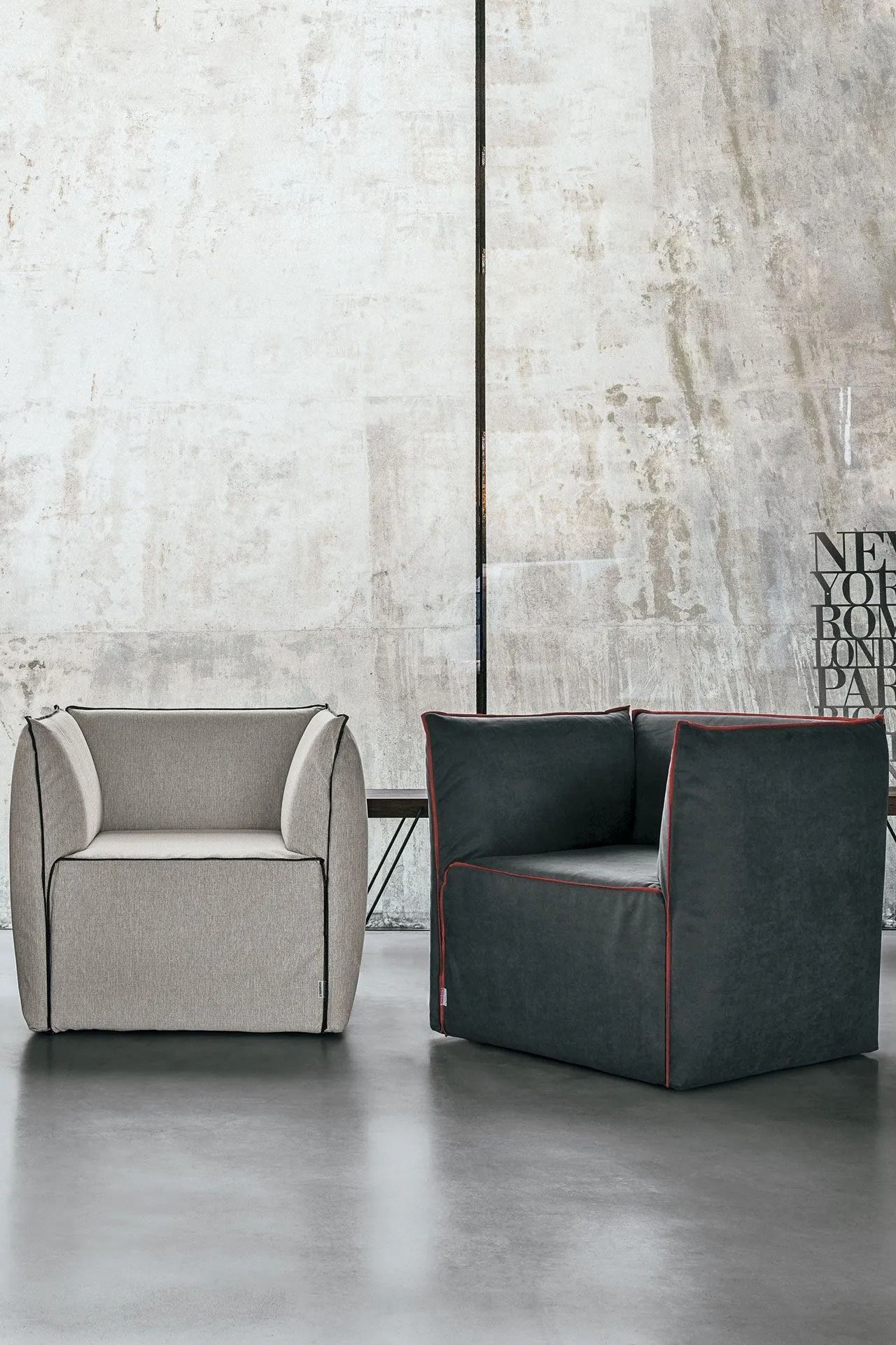 Due poltrone moderne, una grigio chiaro e una grigio scuro, in una stanza minimalista con pareti in cemento.