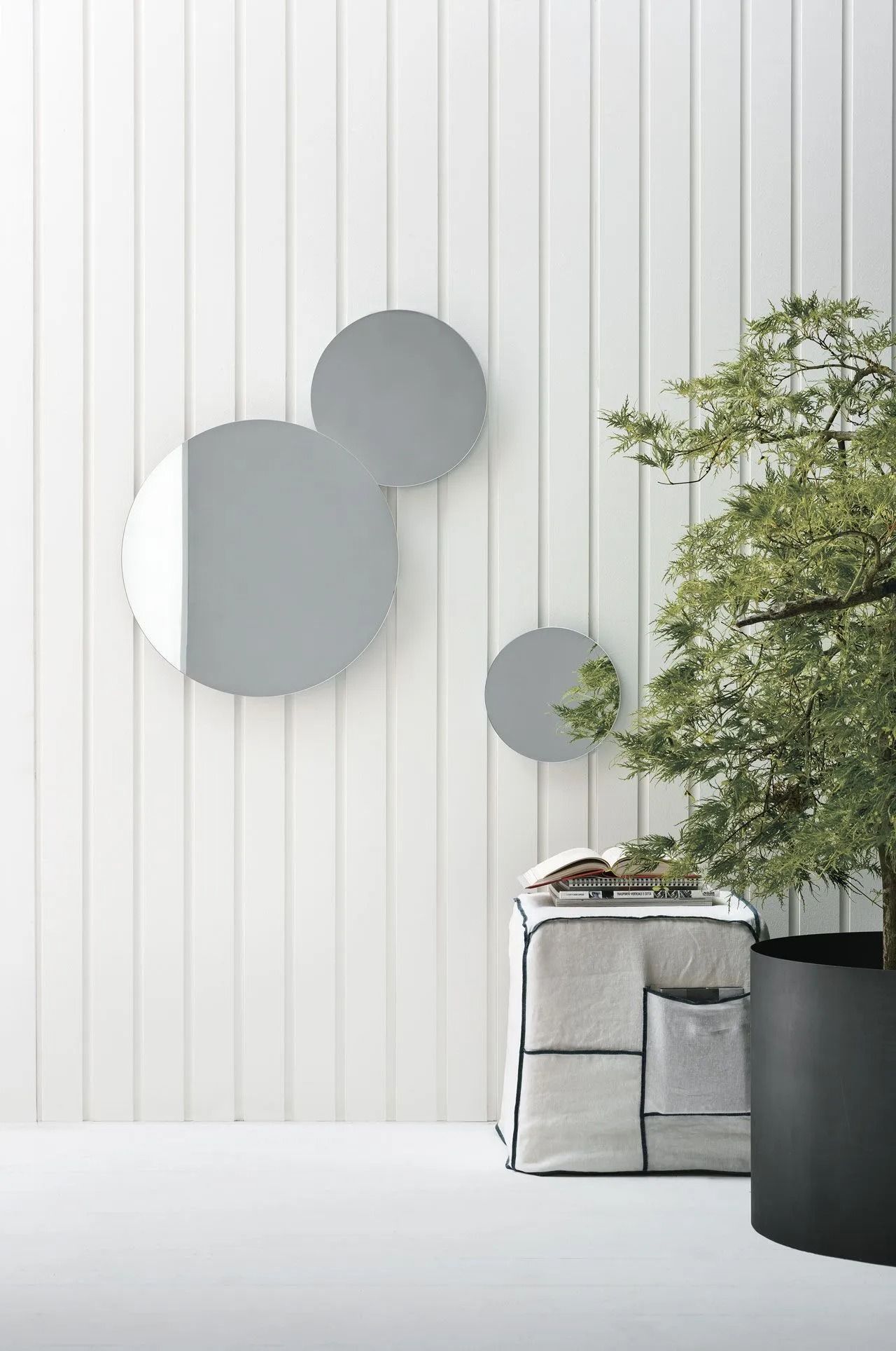 Stanza minimalista con parete rivestita di pannelli bianchi, quadro grigio e pianta in vaso accanto a una panca.
