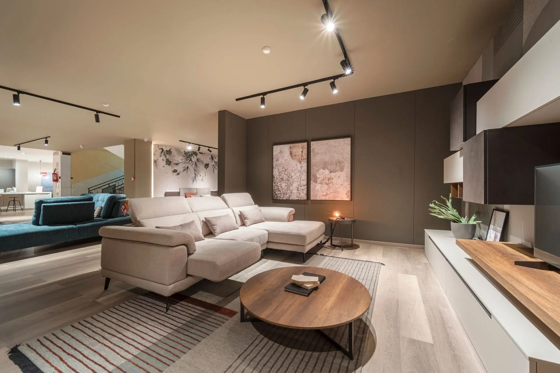 Soggiorno moderno con divano componibile beige, tavolino da caffè in legno, faretti a binario e parete d'accento scura.
