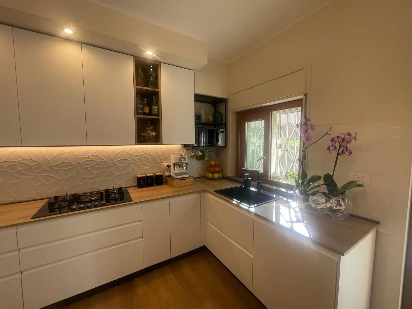 Cucina moderna a forma di L con mobili bianchi, piano di lavoro in legno
