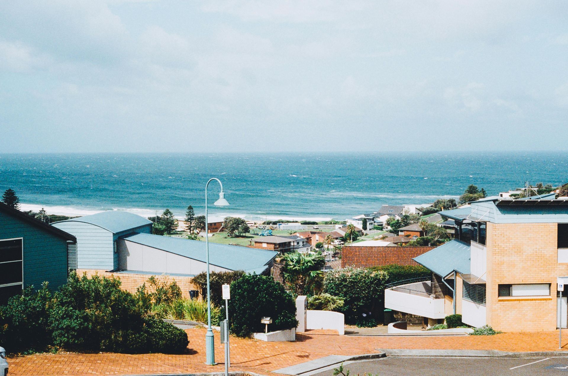 Coastal neighbourhood with colourful houses overlooking a blue ocean and sailboat in the distance