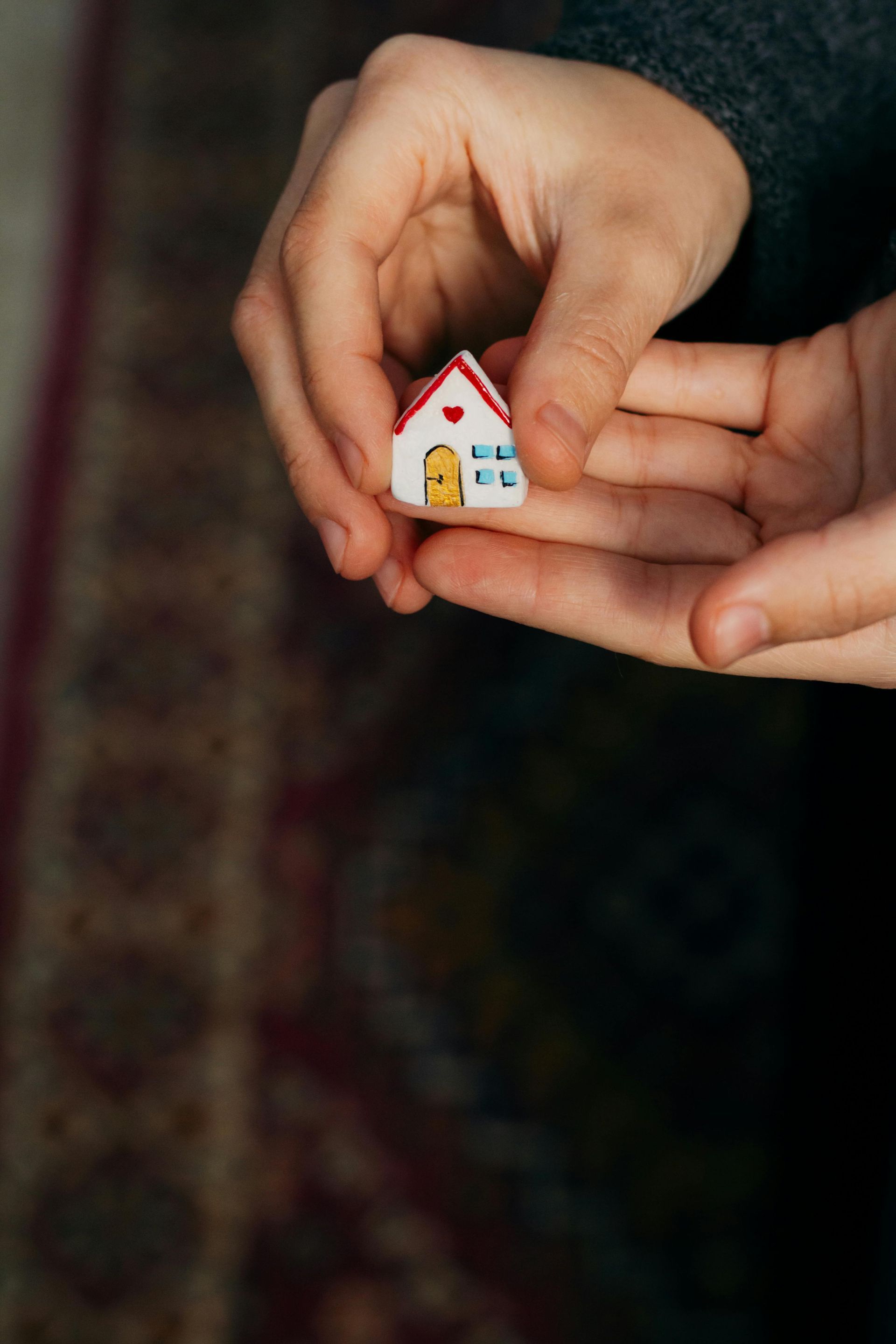 Hands holding a tiny white toy house with a red roof and yellow door.