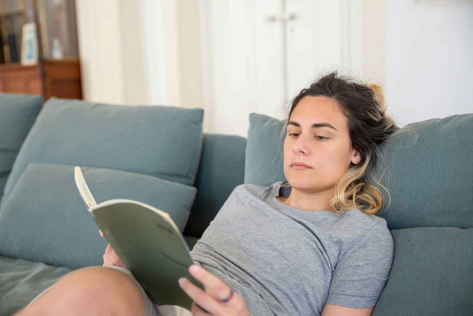 Person reading a book on a blue sofa in a bright living room