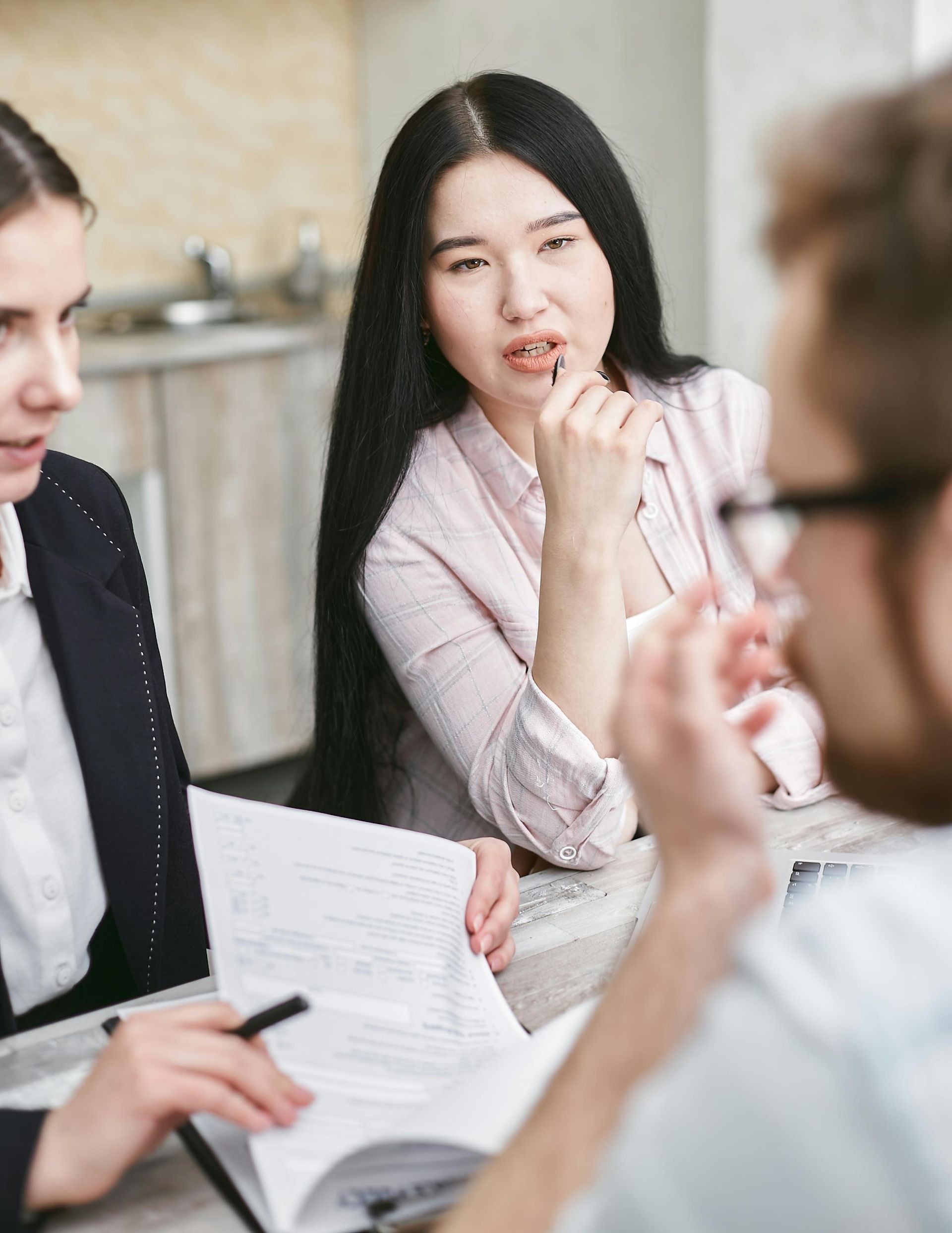 Three people in a meeting, discussing papers around a table in a bright office.