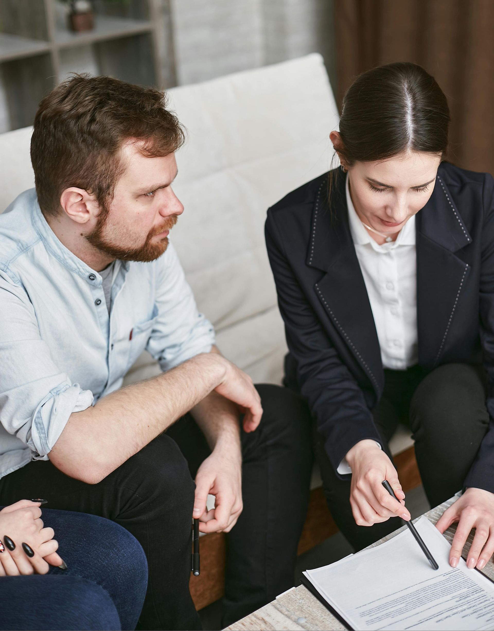 Two people discussing documents on a couch, with one pointing at a clipboard.