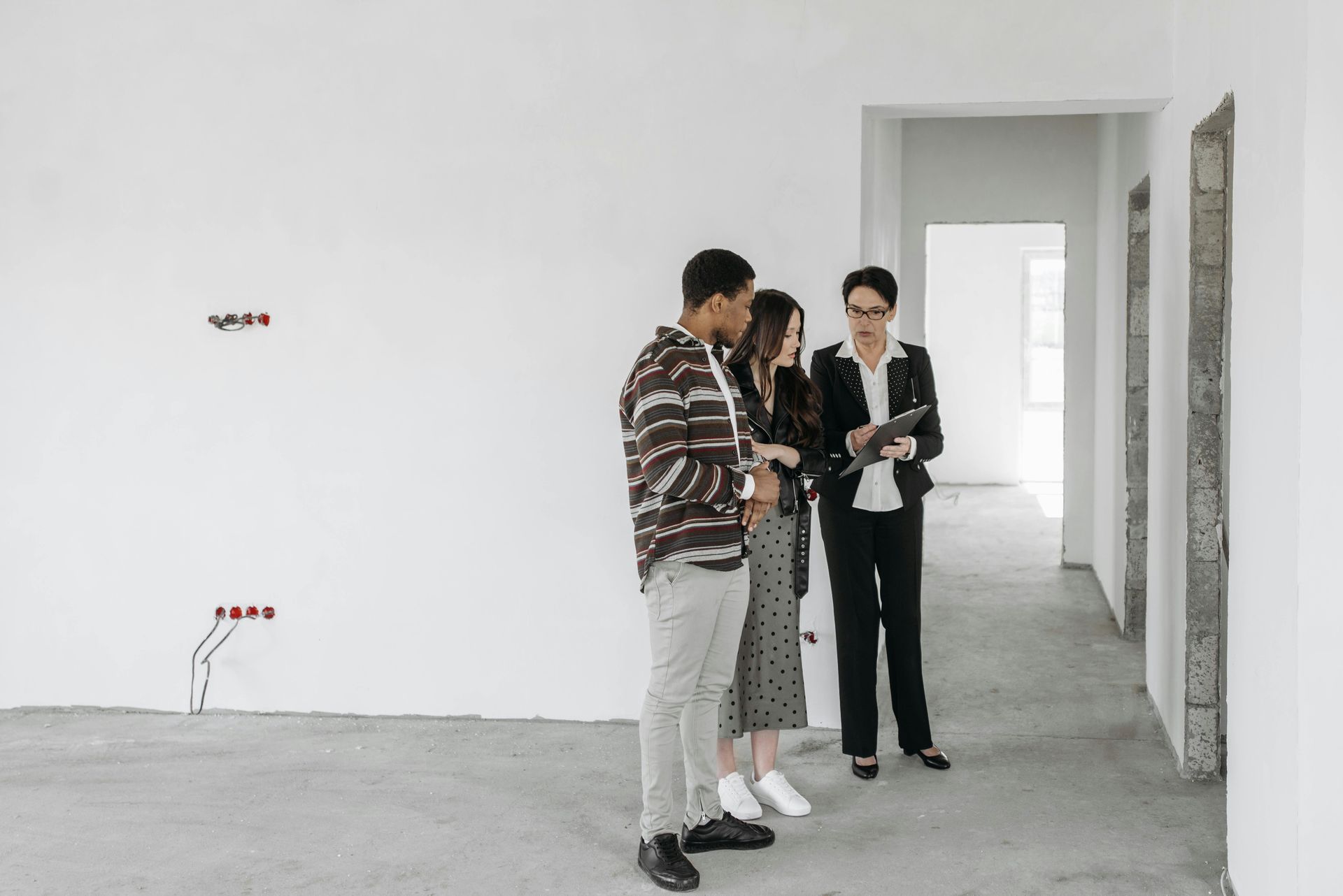 Three people stand in a bare room, looking at a tablet and discussing the space.