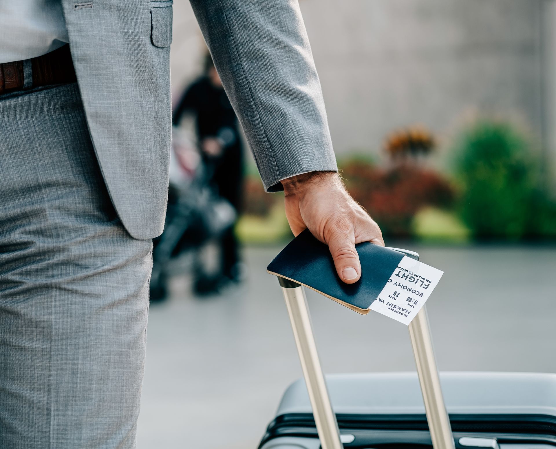 A man in a suit is holding a passport and a suitcase.