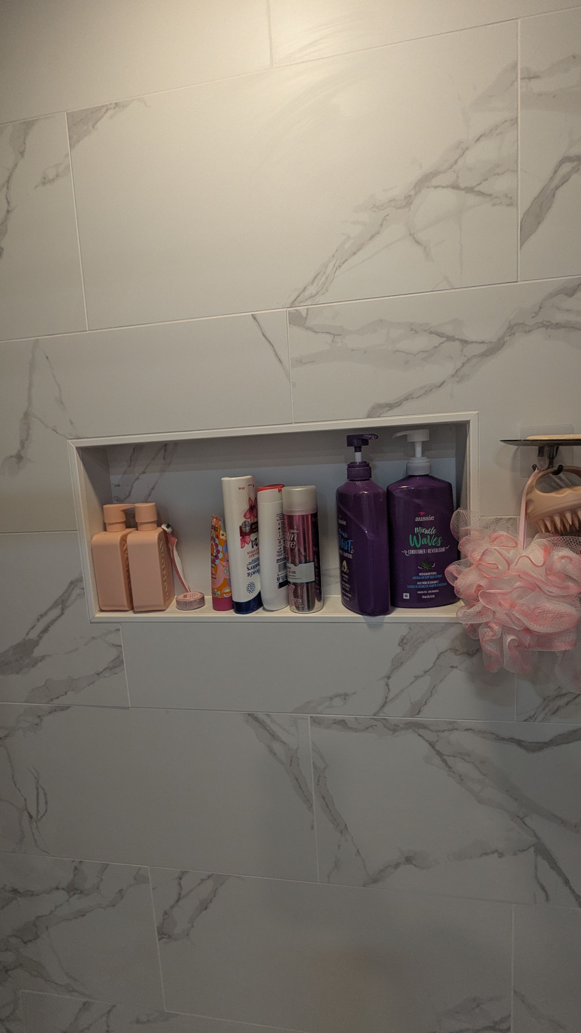 Mur carrelé de blanc avec une étagère encastrée contenant des flacons de shampoing, d'après-shampoing et de gel douche.