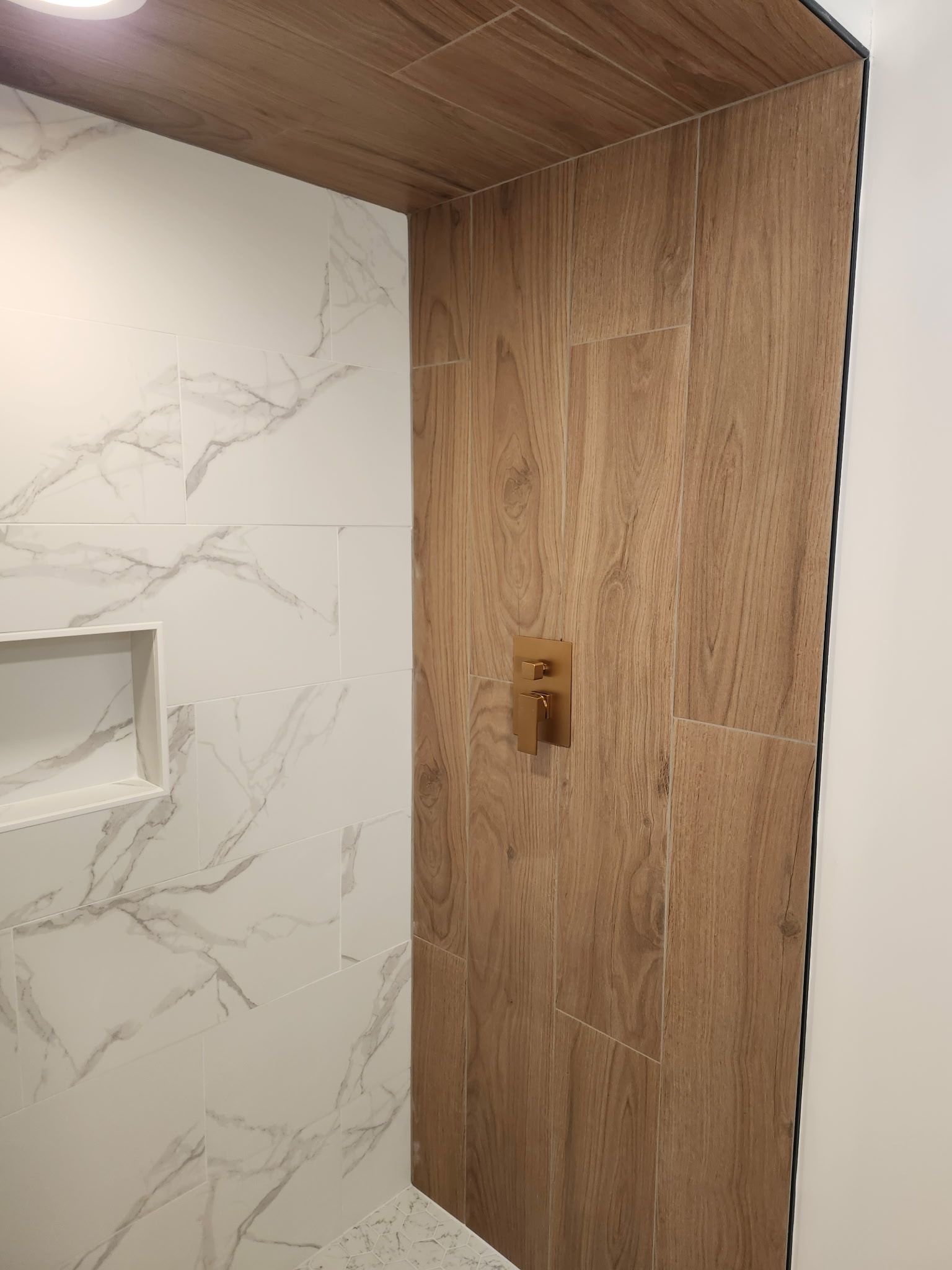 Douche avec carrelage imitation bois sur un mur, carrelage imitation marbre sur un autre et étagère encastrée.
