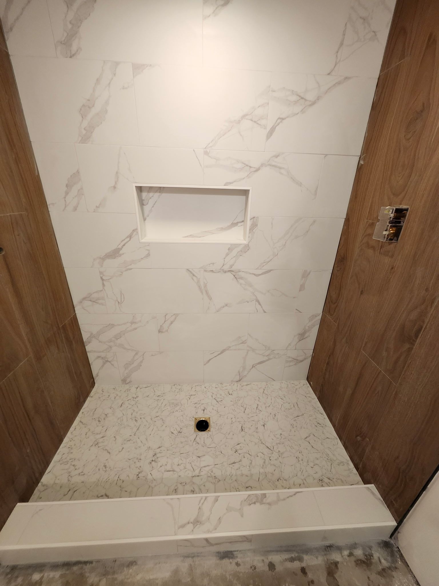 Cabine de douche avec murs carrelés de marbre blanc et étagère encastrée.