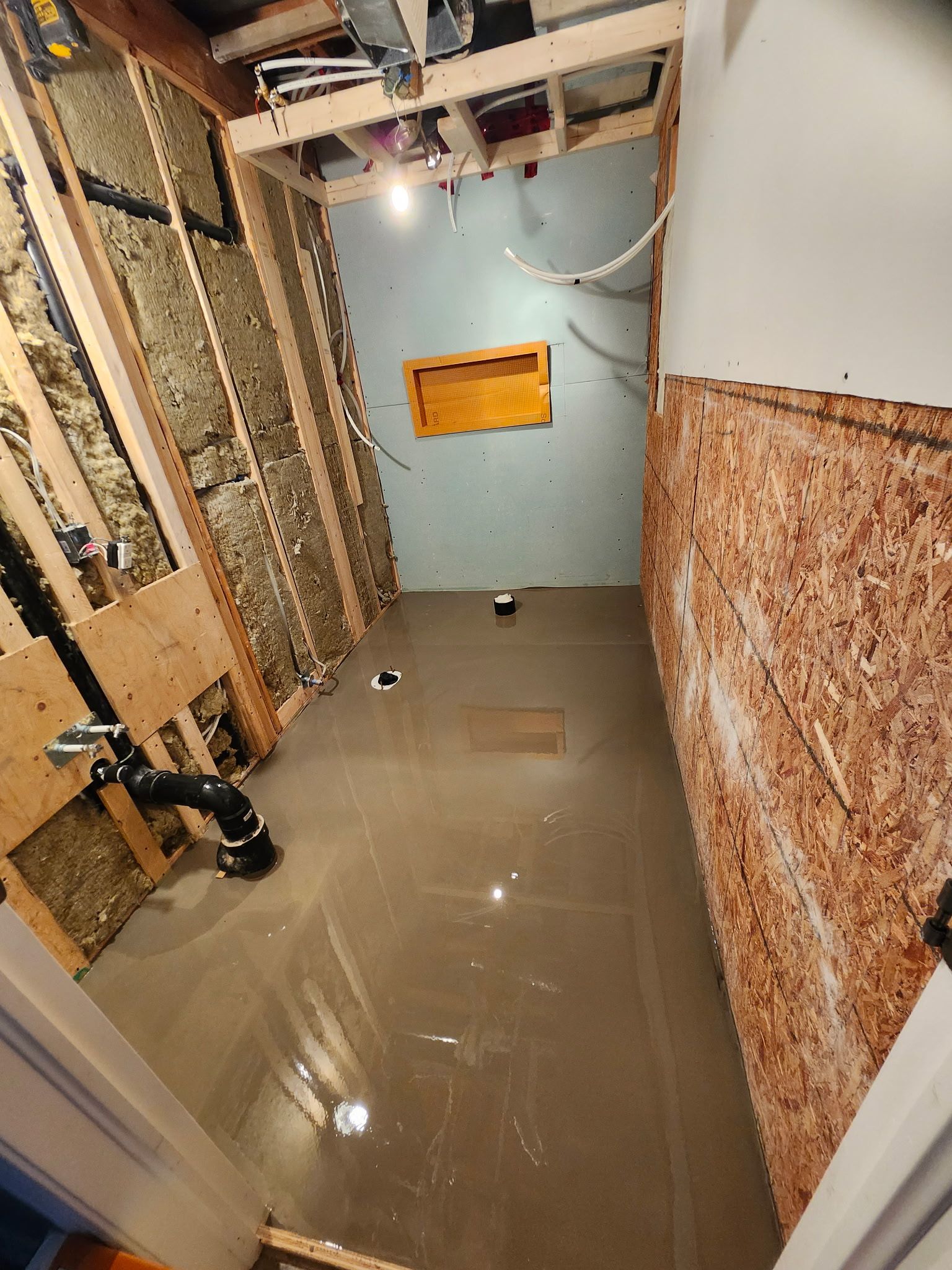 Salle de bains en construction avec charpente apparente, isolation et sol en béton.