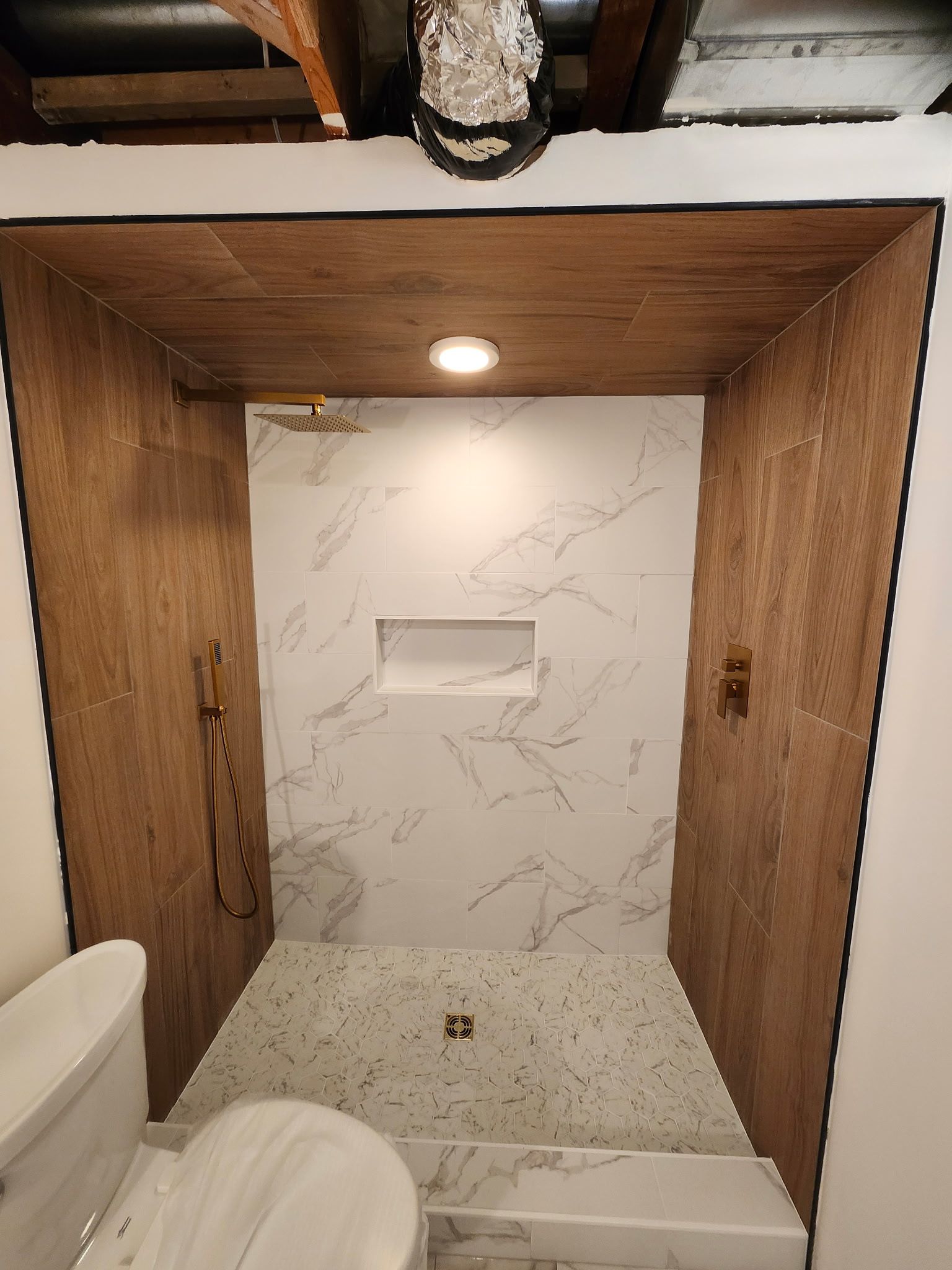 Salle de bains moderne avec douche en marbre, robinetterie dorée et éléments en bois.