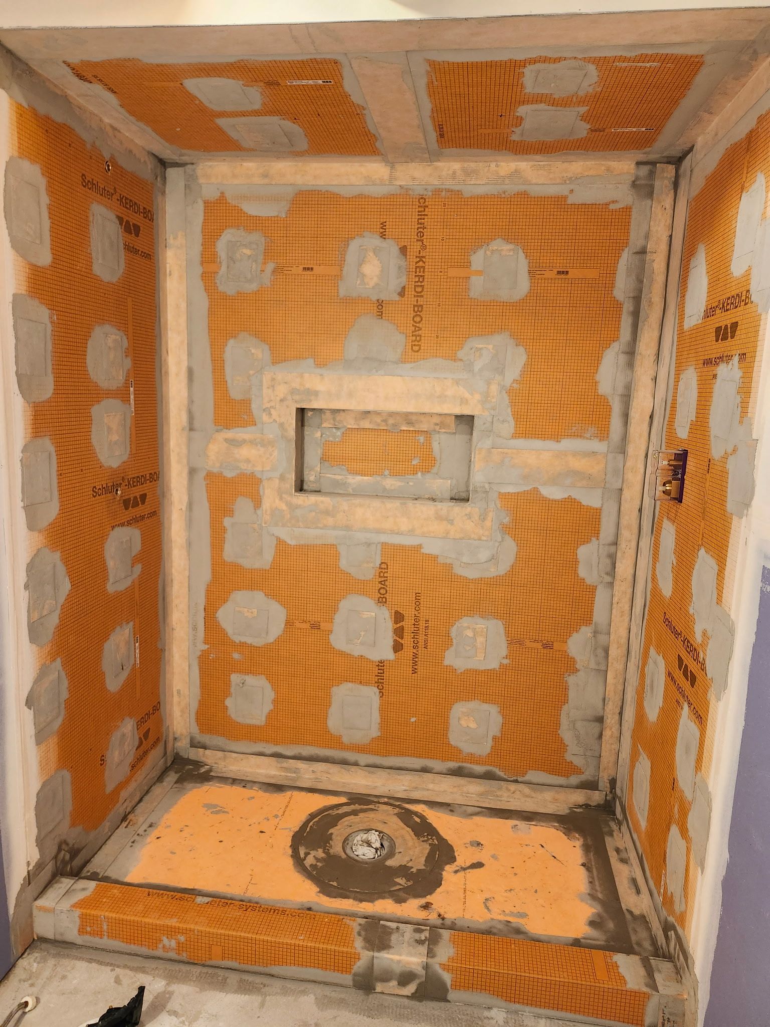 Cabine de douche en construction, membrane d'étanchéité orange avec mortier gris appliqué, bonde visible.