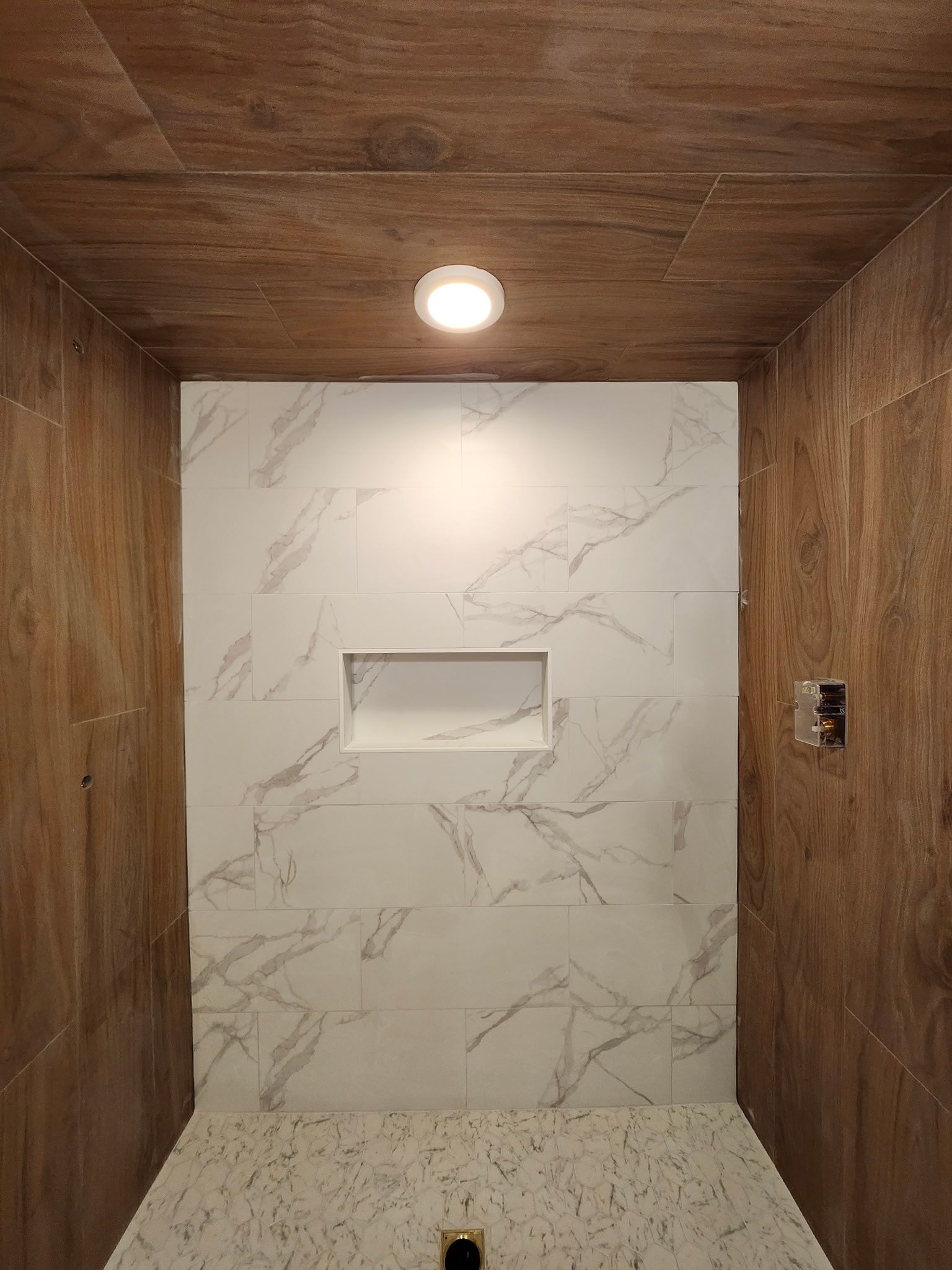 Intérieur de douche avec mur aspect marbre, parois latérales et plafond aspect bois, niche et éclairage encastré.