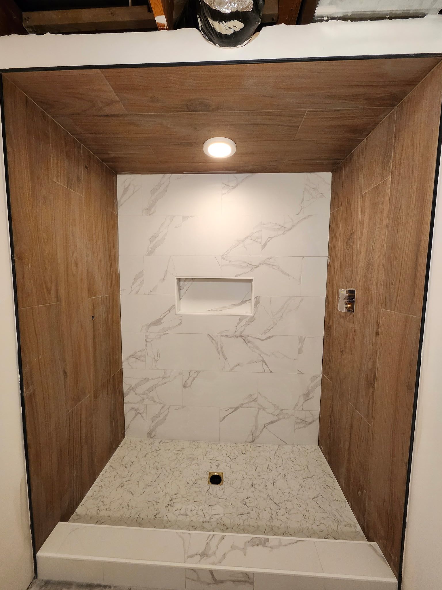 Douche récemment rénovée avec murs carrelés bruns, mur d'accent en marbre blanc, niche encastrée et sol carrelé gris.