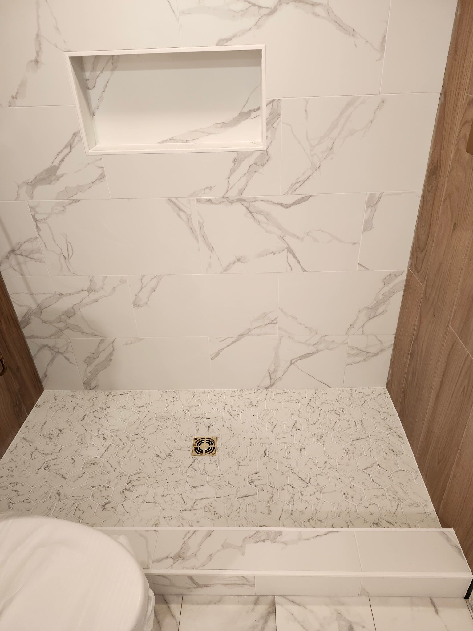 Salle de douche avec carrelage blanc imitation marbre et étagère encastrée. Le sol de la douche présente un motif moucheté.