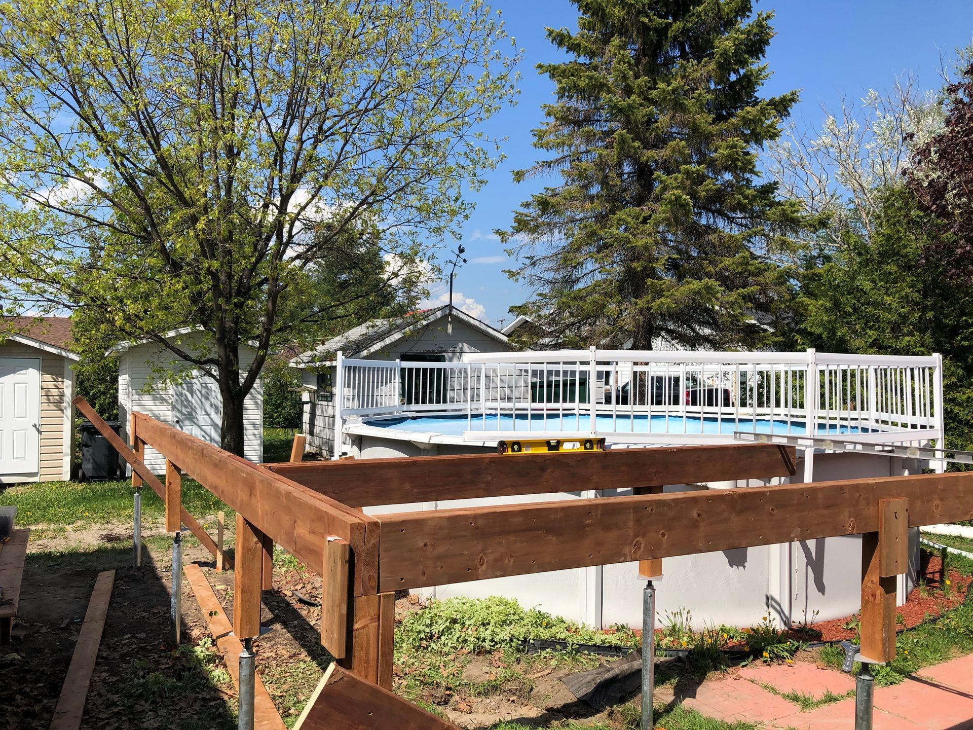 Construction d'une terrasse en bois à ossature autour d'une piscine hors sol dans un jardin, par une journée ensoleillée.
