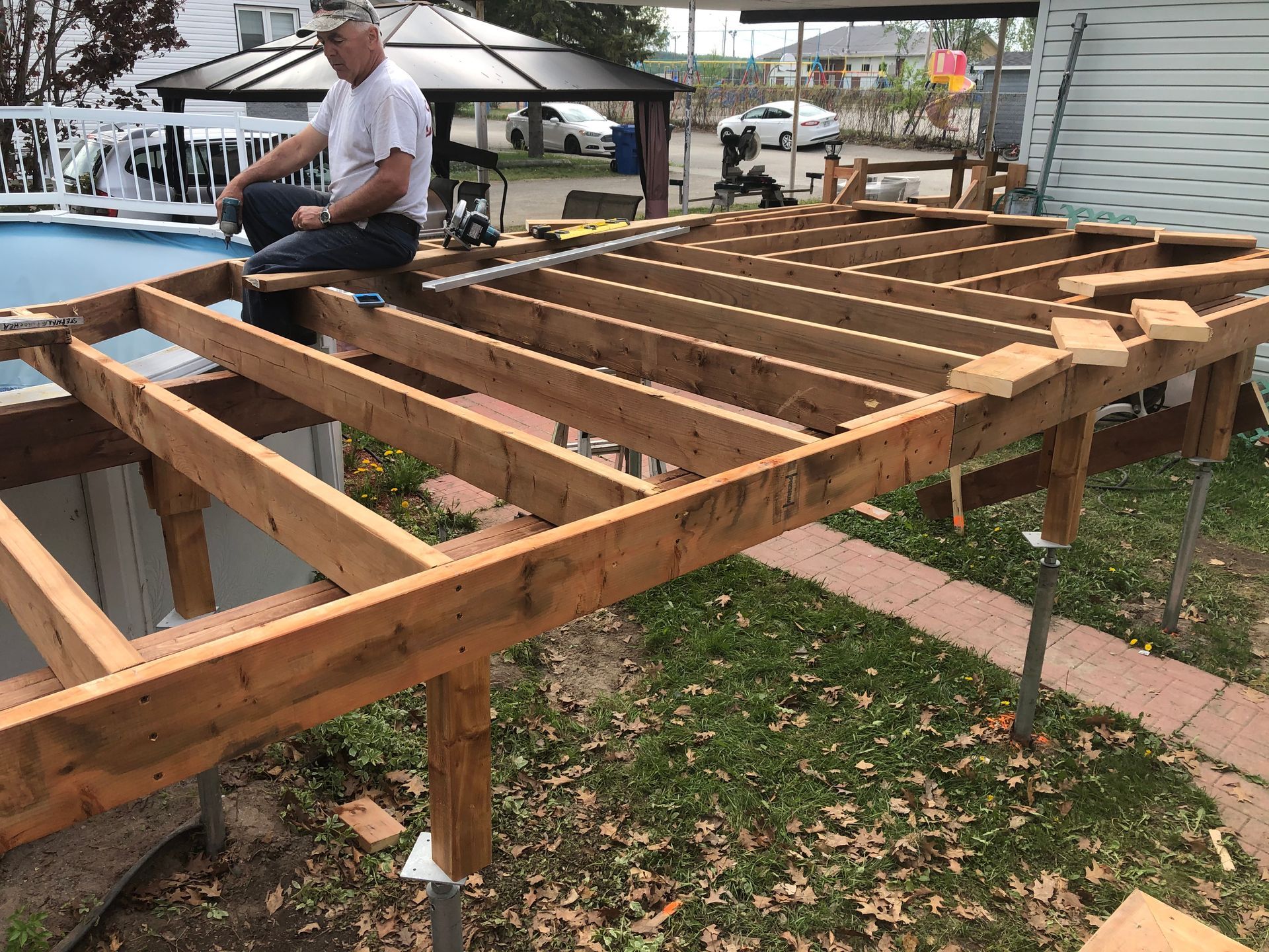 Un homme travaille sur une terrasse en bois partiellement construite près d'une piscine.